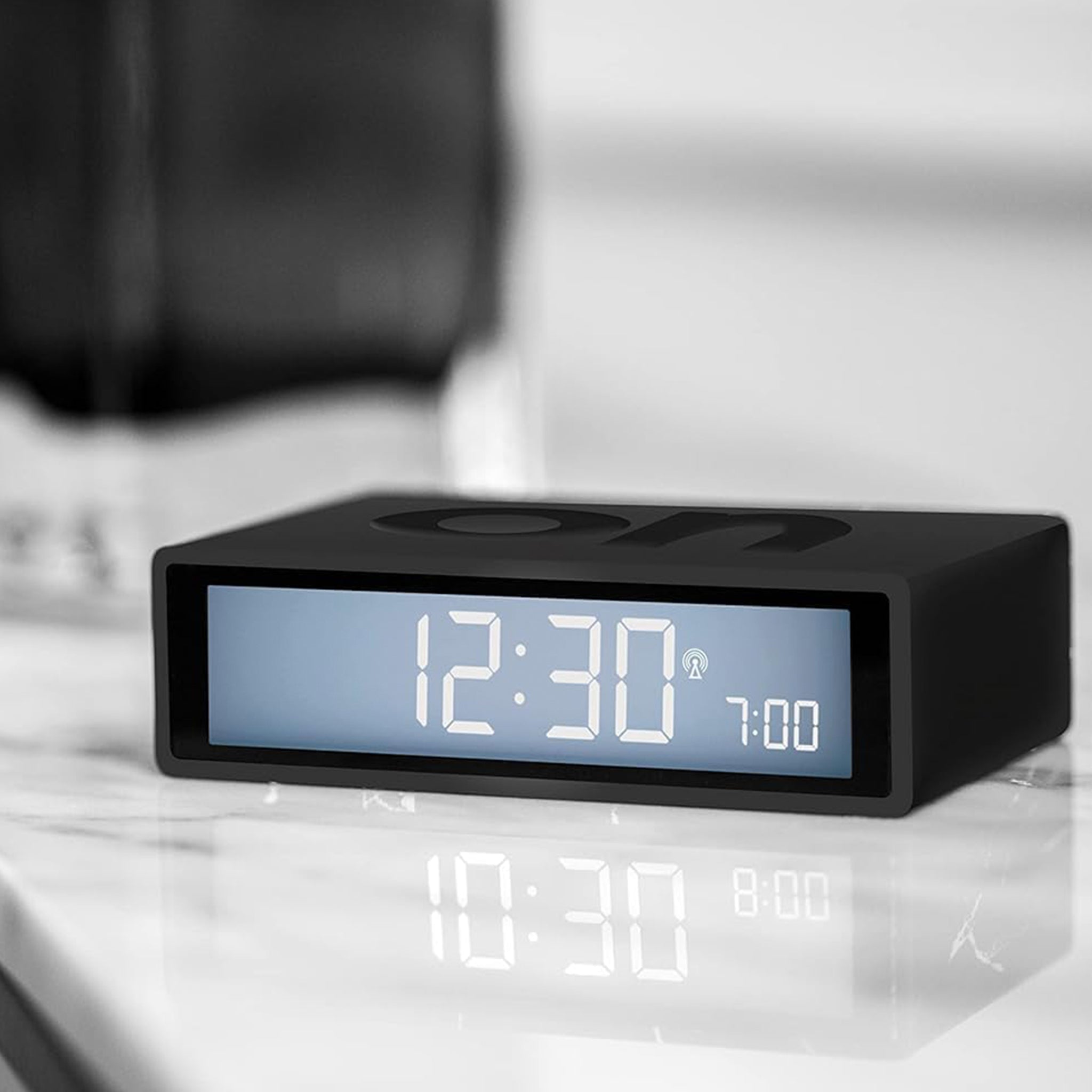 Black digital clock with LED display on a reflective surface