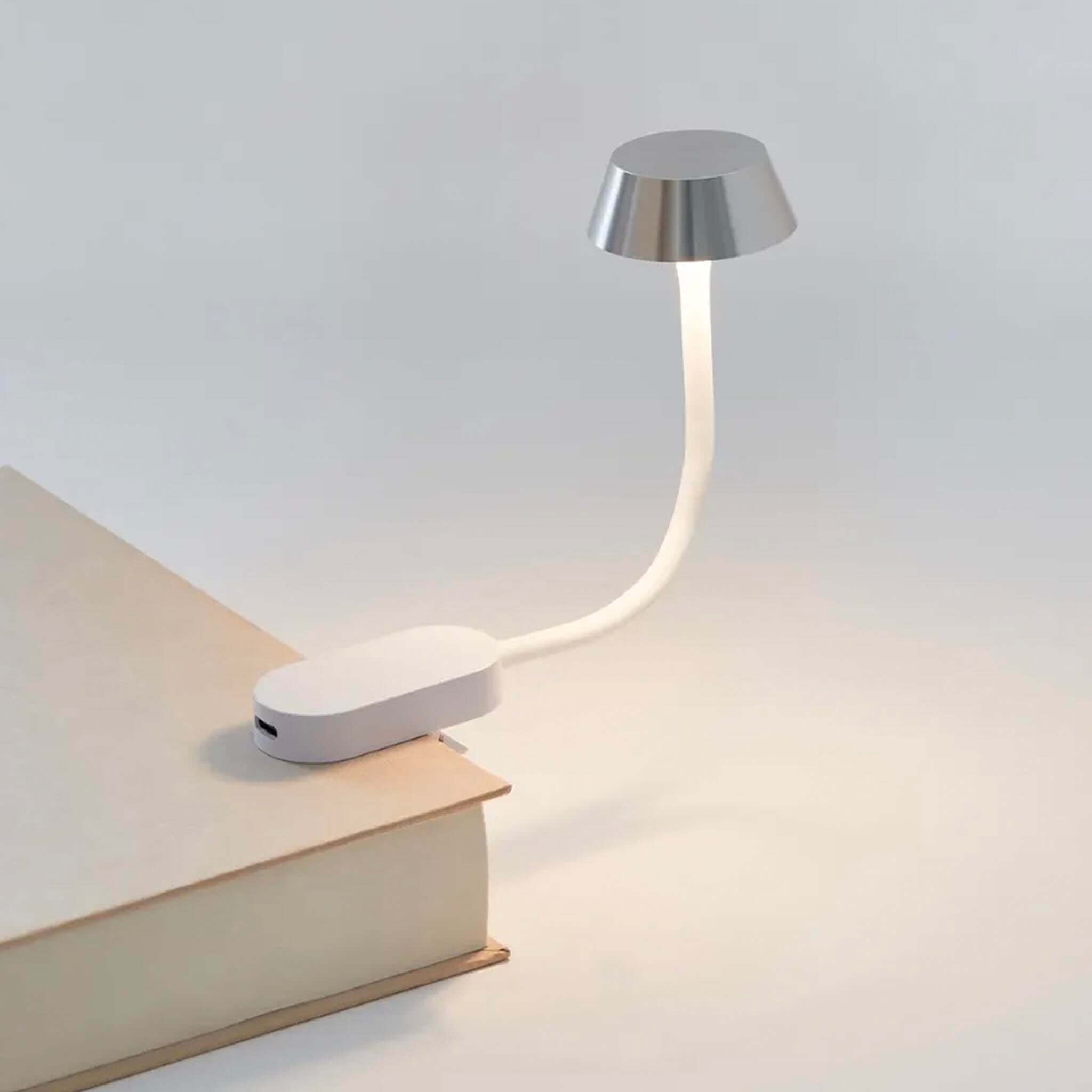 Small LED desk lamp with flexible neck on a book against a light gray background