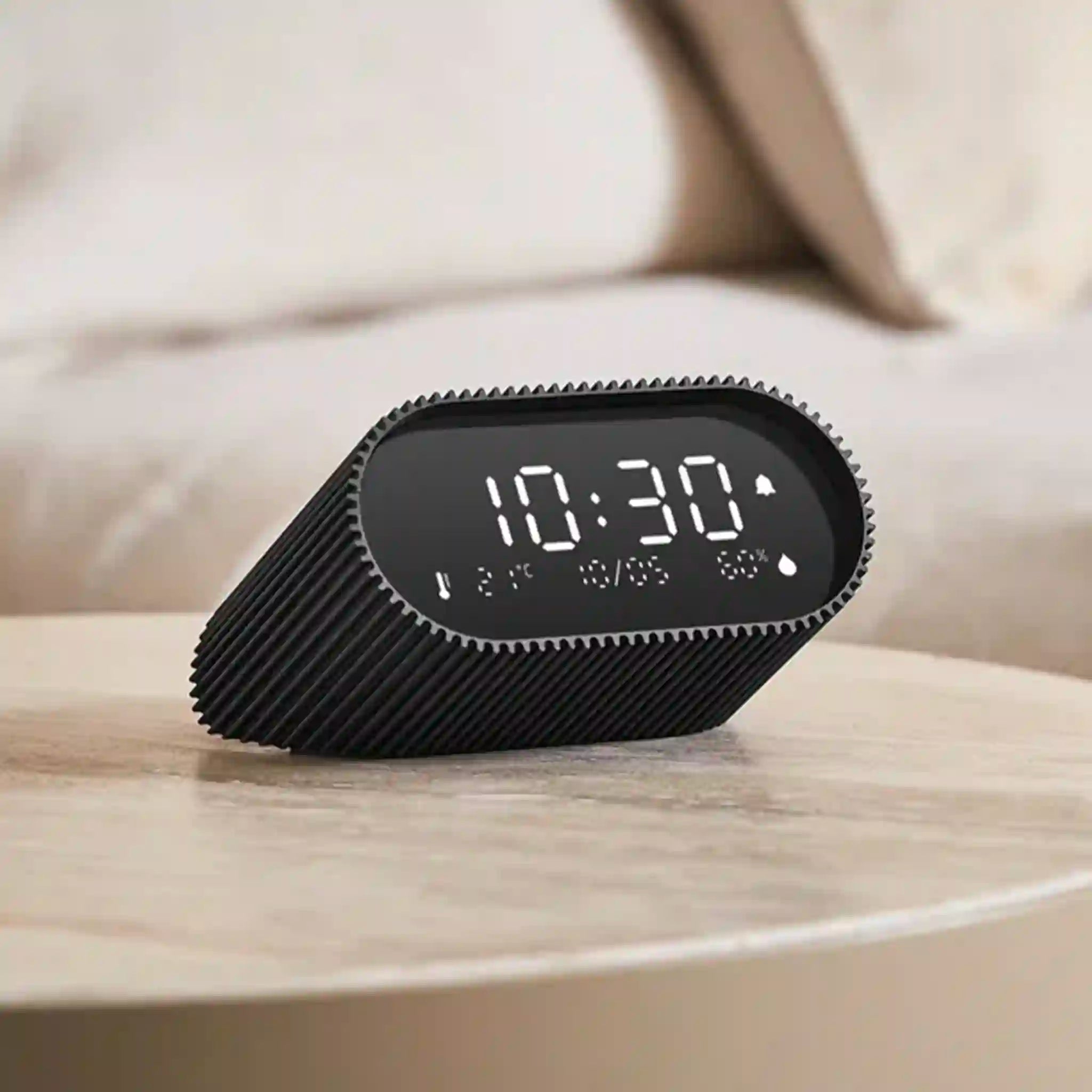 Black digital clock on a wooden surface with a blurred background