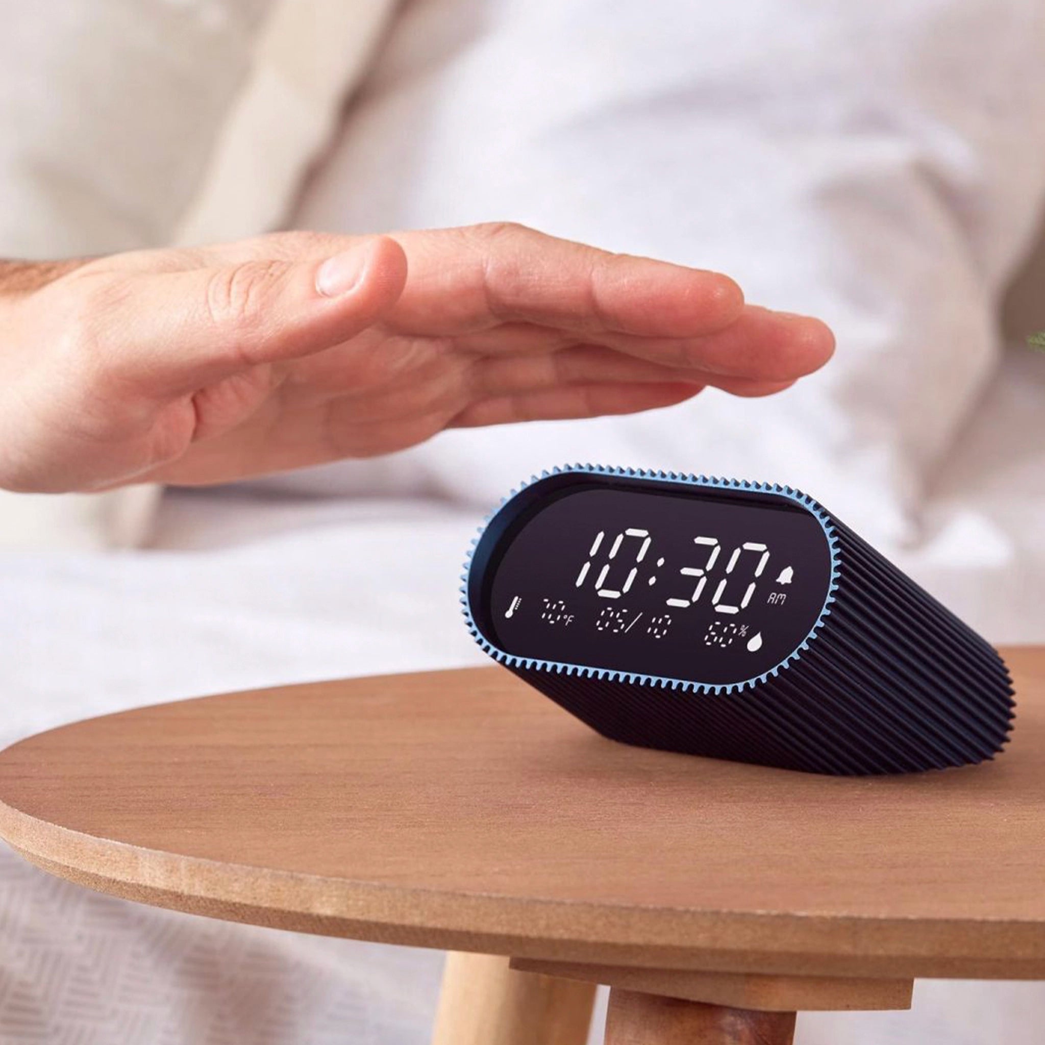Hand over a digital clock with a textured blue casing on a side table.