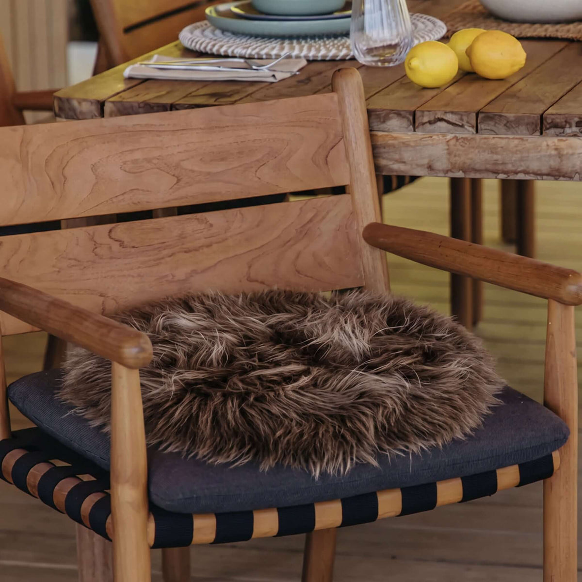 Long Wool Sheepskin Circle Chair Pad - Taupe on a wooden chair with a dark cushion, enhancing home decor.