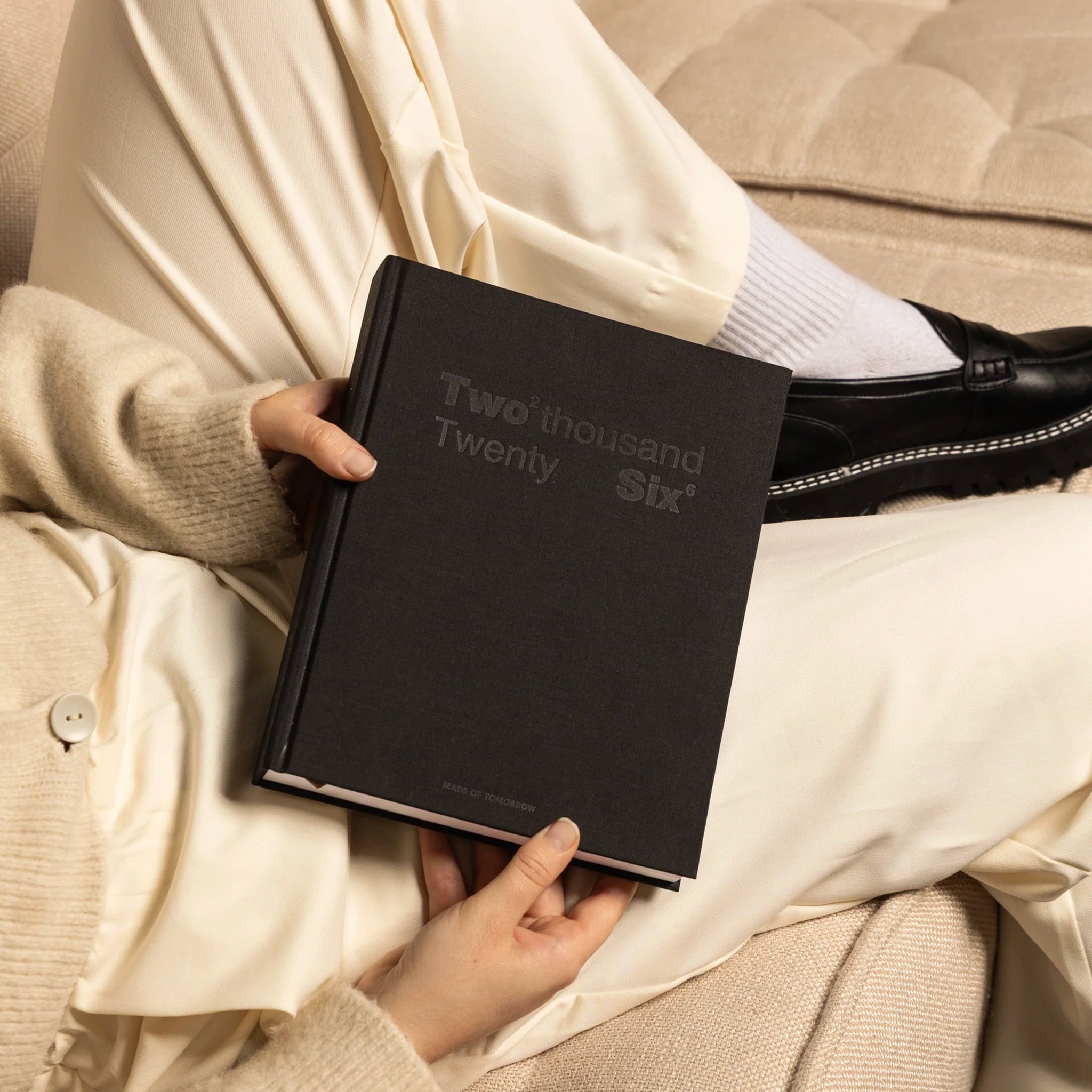 Person holding a black notebook titled 'Two thousand Twenty Six' on a neutral background