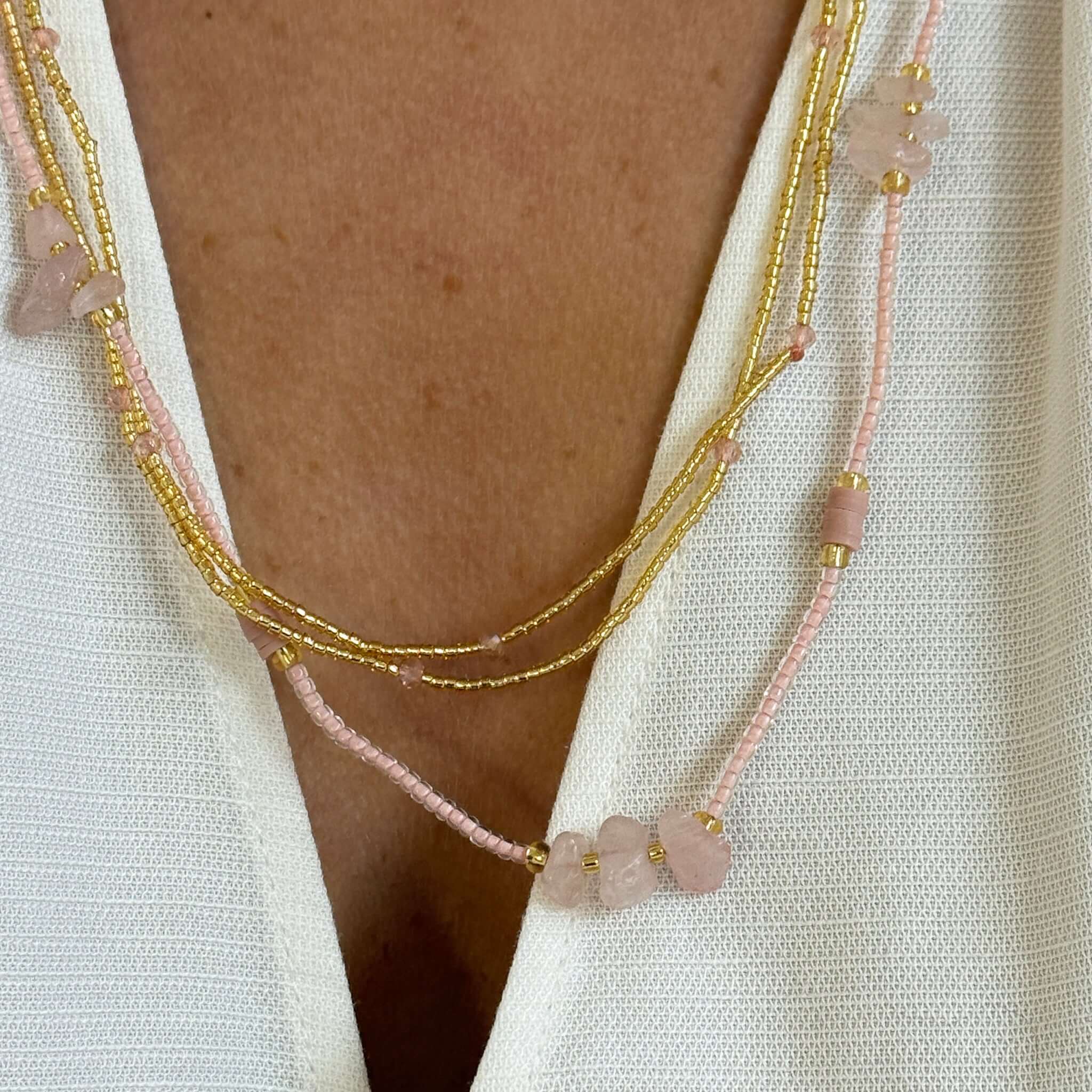 Margaret Dorothy Necklace featuring gold seed beads and pink accent beads layered on a white top.