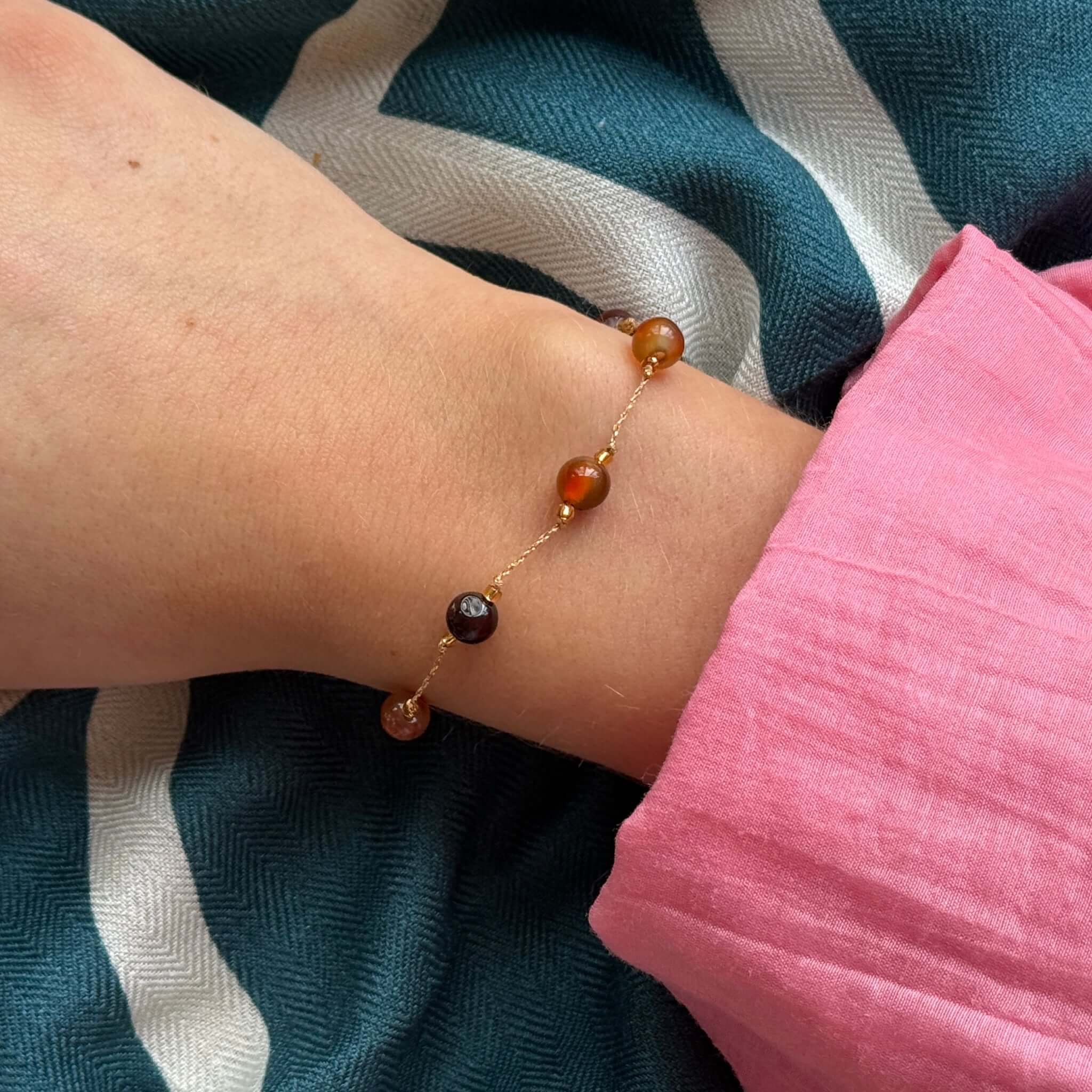 Margaret Loretta Bracelet featuring round stone beads on a gold metallic cord, showcased on a wrist.