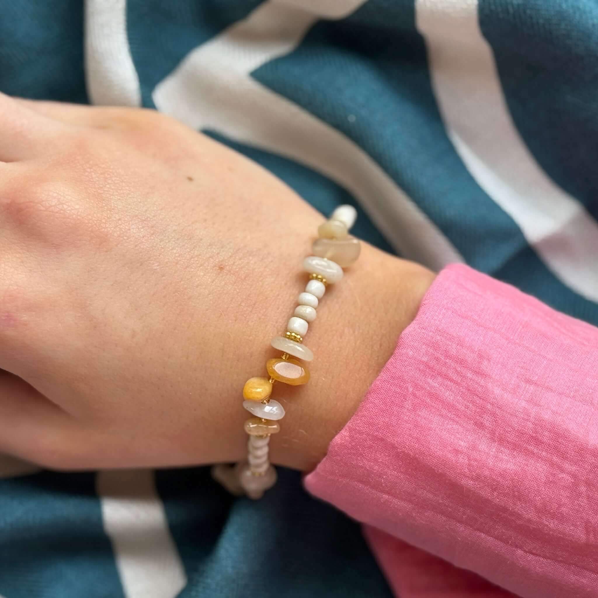 Margaret Marie Bracelet - Sand & Amber featuring pale ceramic beads and natural stone chips worn on a hand with a pink shirt.