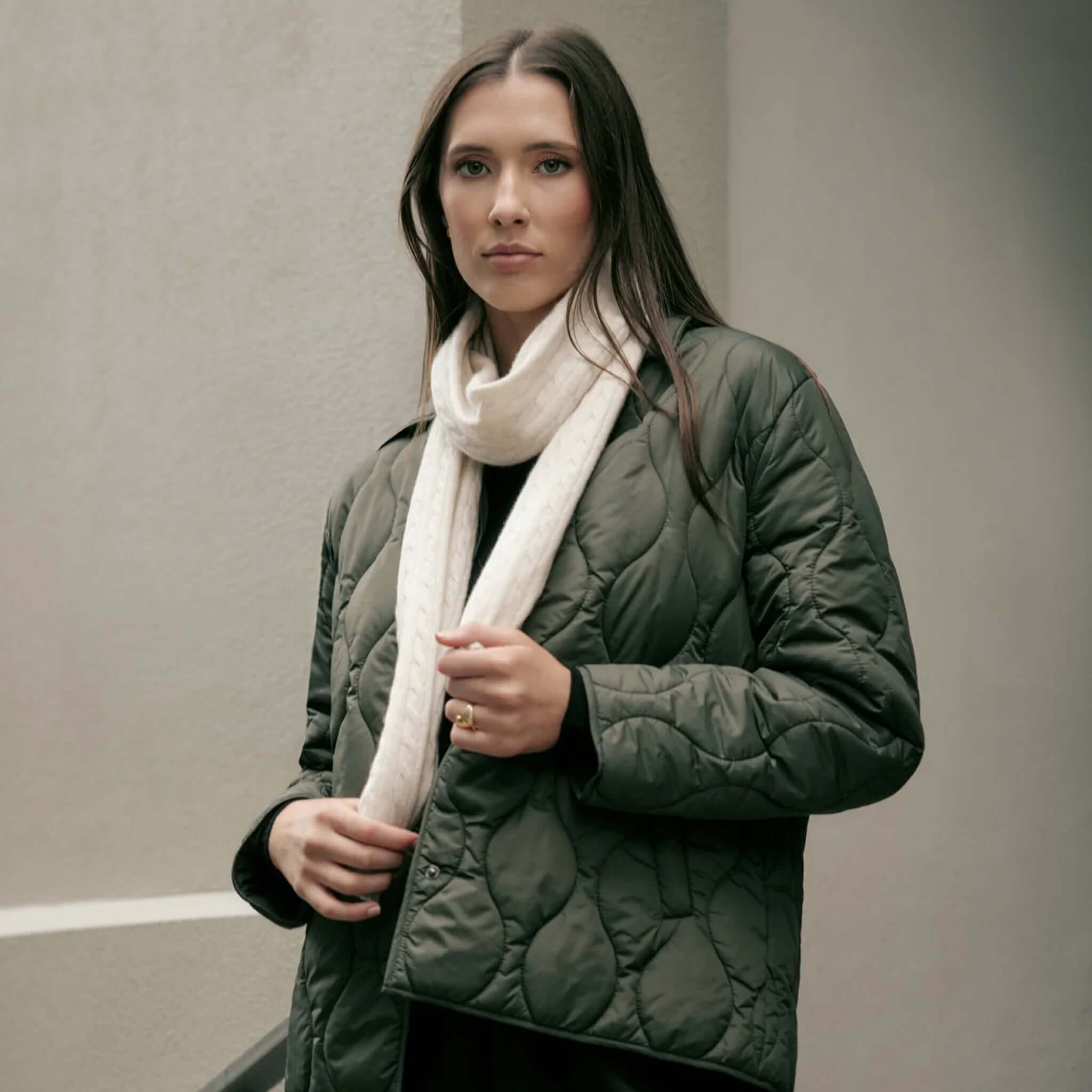 Woman wearing the Marlow Toronto Quilted Jacket - Spruce with a white scarf against a minimal backdrop.