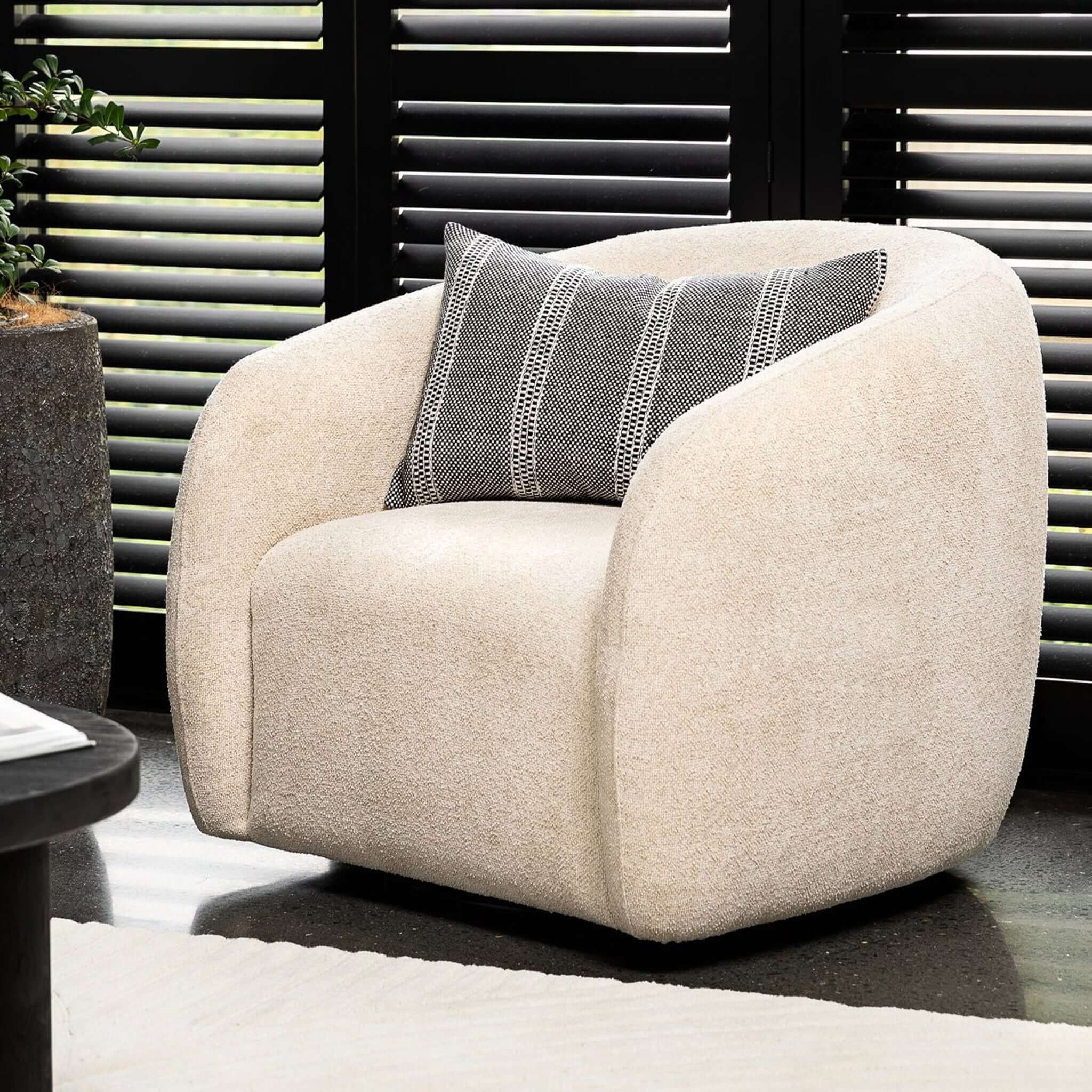 Alt Tag: Max Swivel Chair in cream boucle with curved arms, supportive high back and roomy seat, styled with striped cushion