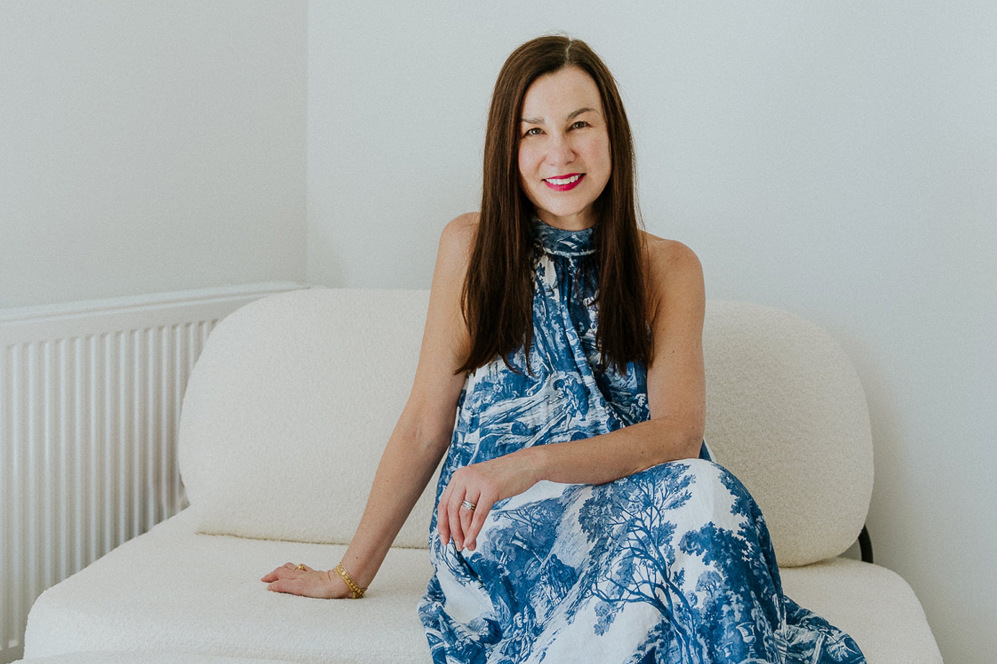 Woman in a blue and white dress sitting on a white couch against a white wall.