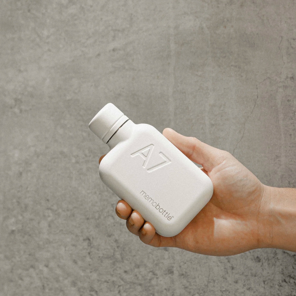 Memobottle A7 Stainless Steel - White held in hand against a concrete wall