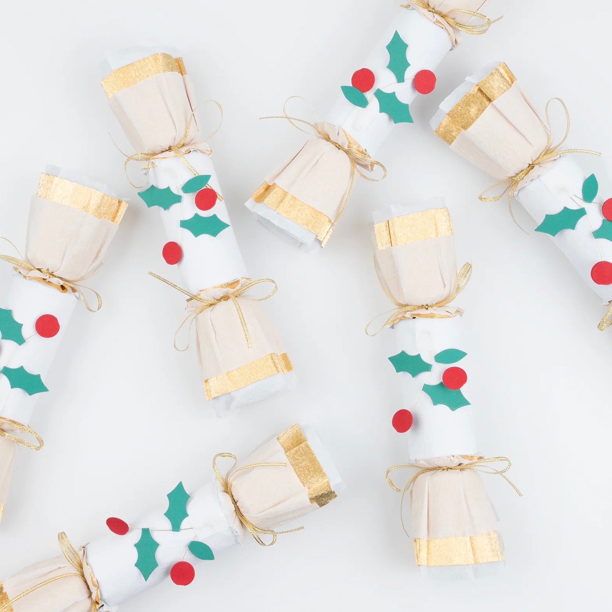 A set of six Christmas crackers with gold ribbon bows, white crepe paper layers, and red and green holly leaves and berries.