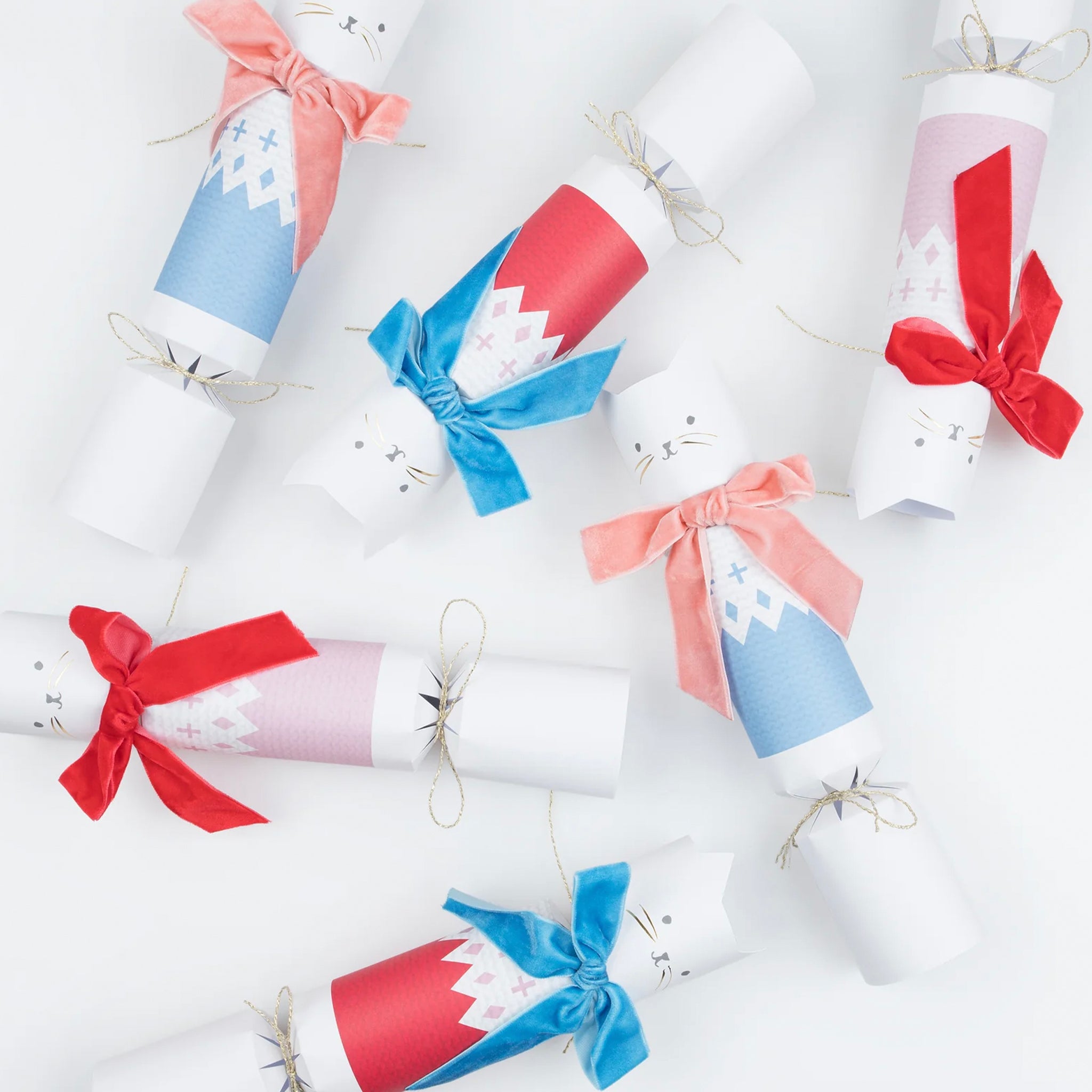 A set of six Christmas crackers with cat designs, featuring velvet bows and fair isle knitwear in dusty pink, red, and light blue colors.