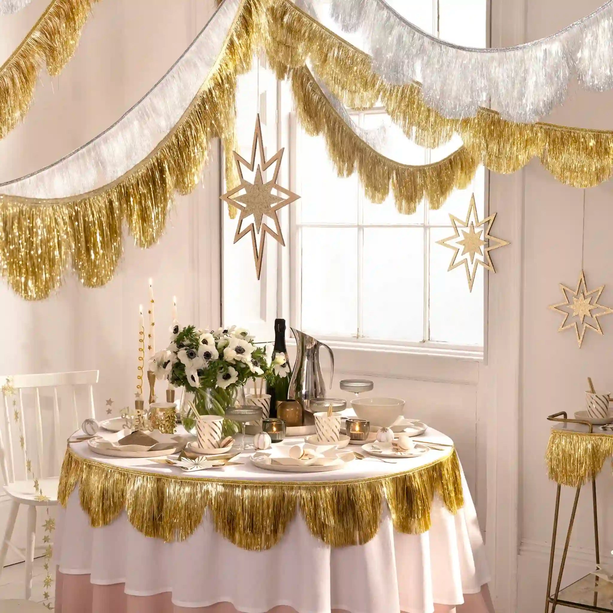 Decorated table with gold fringe tablecloth and white tablecloth, surrounded by festive decorations.