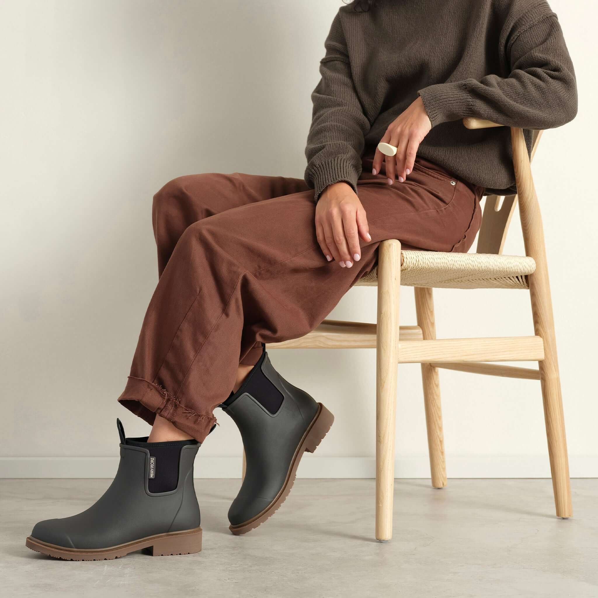 Merry People Bobbi Ankle Boots - Charcoal worn by a model sitting on a chair, showcasing comfort and style.