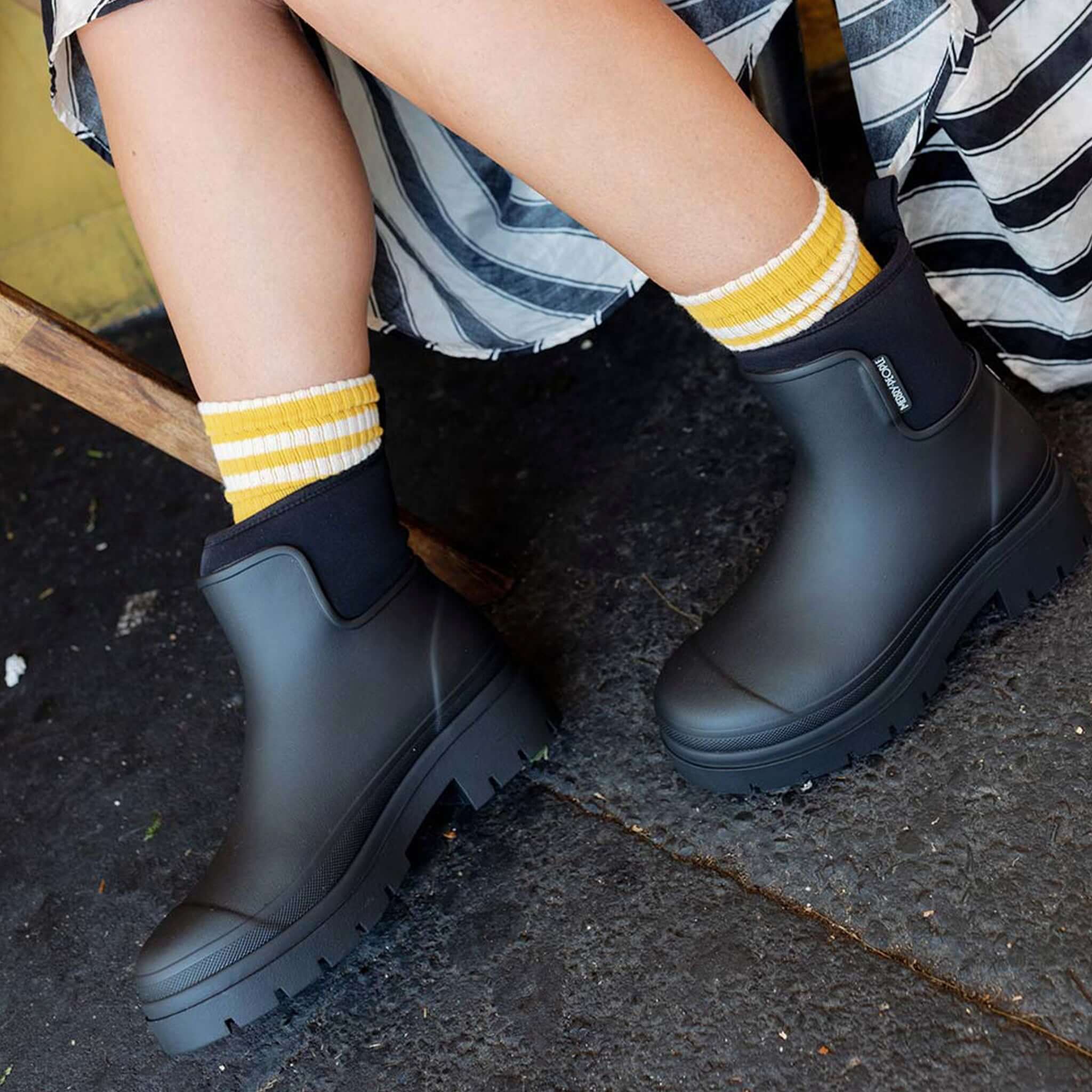 Alt Tag: Merry People Tully Boots - Black chunky platform waterproof gumboots with neoprene cuff, worn with striped socks