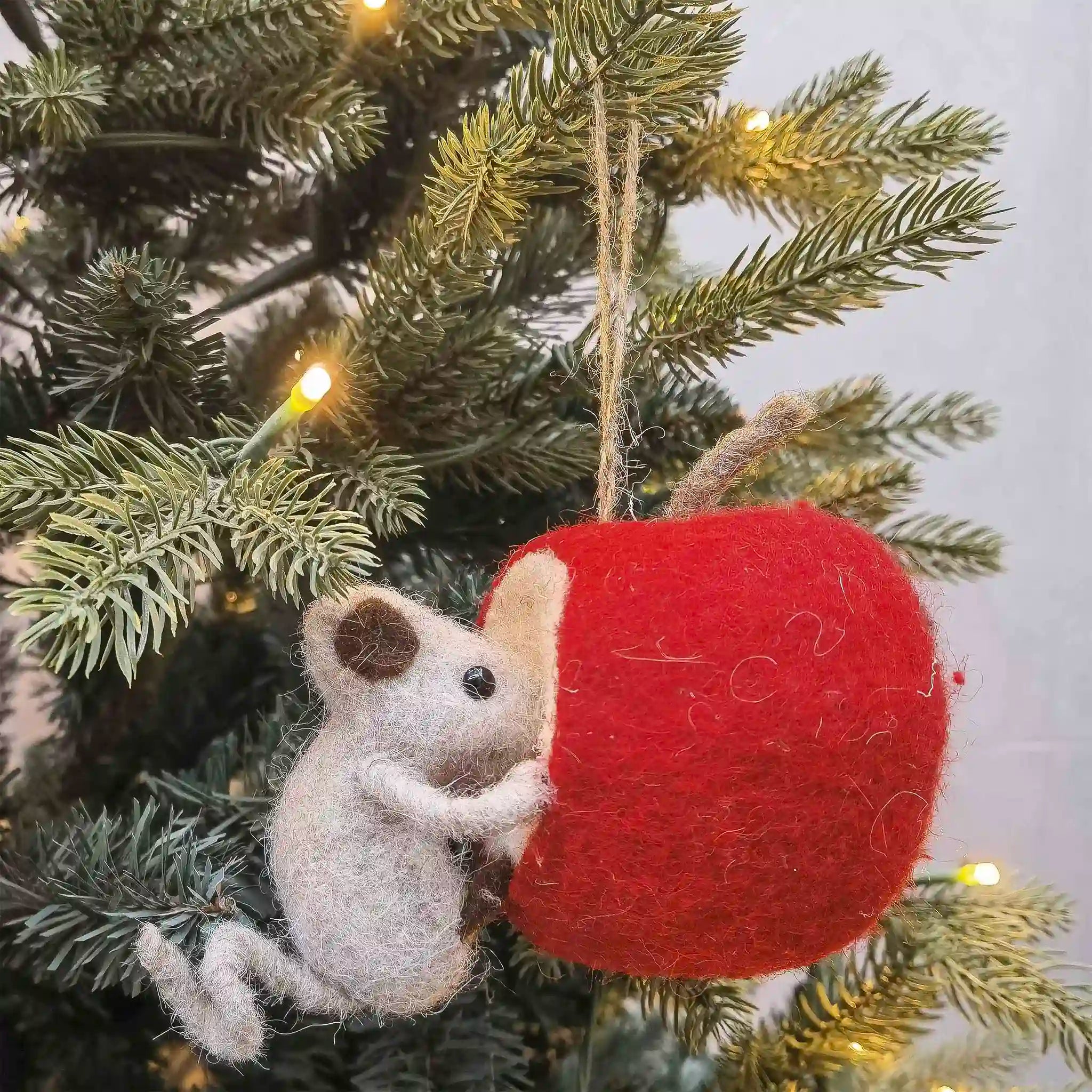 Felted mouse ornament peeking out from a red ball hanging on a Christmas tree.