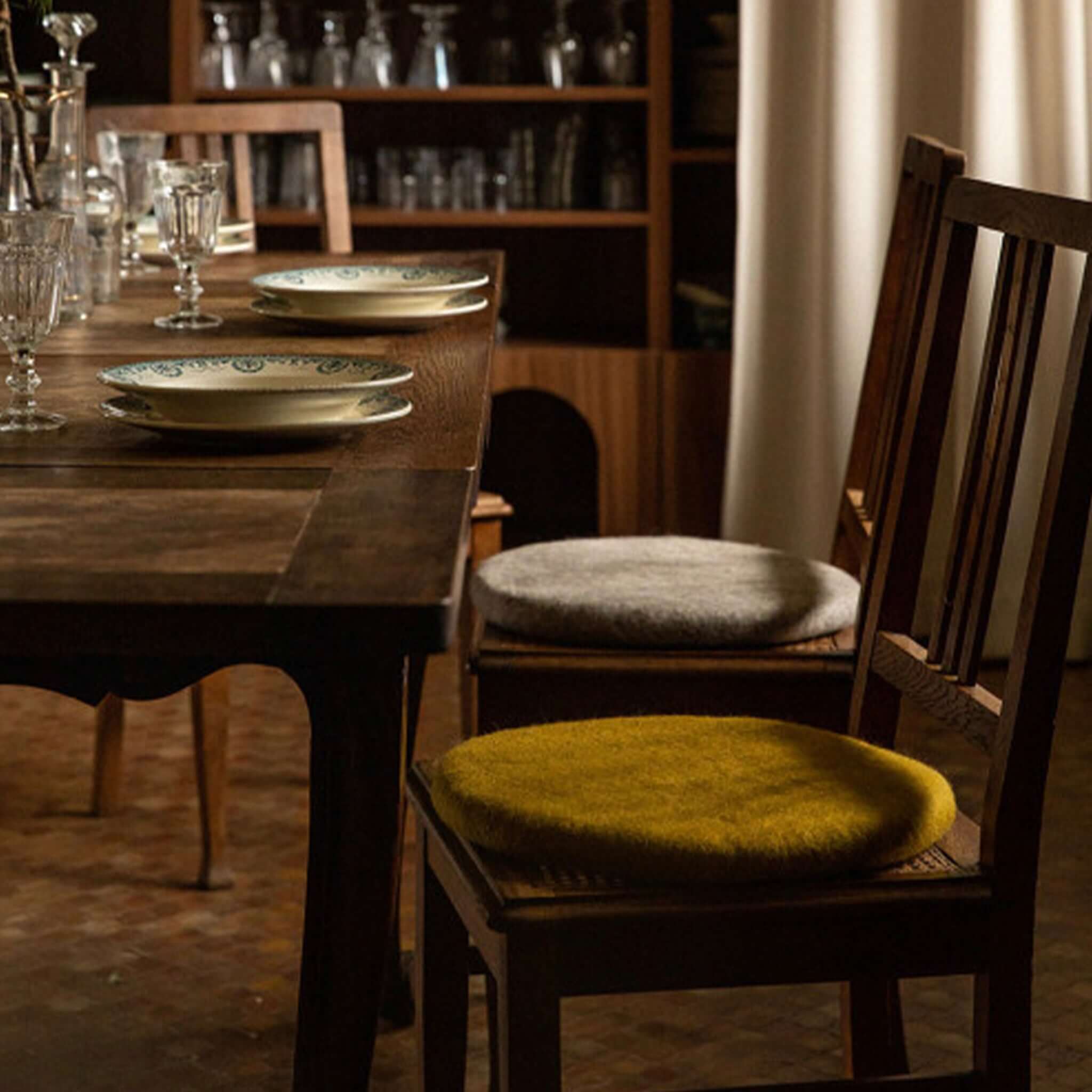 Muskhane Felt Chakati Cushion - Pistachio on wooden dining chair, round felt wool seat pad in warm dining room setting