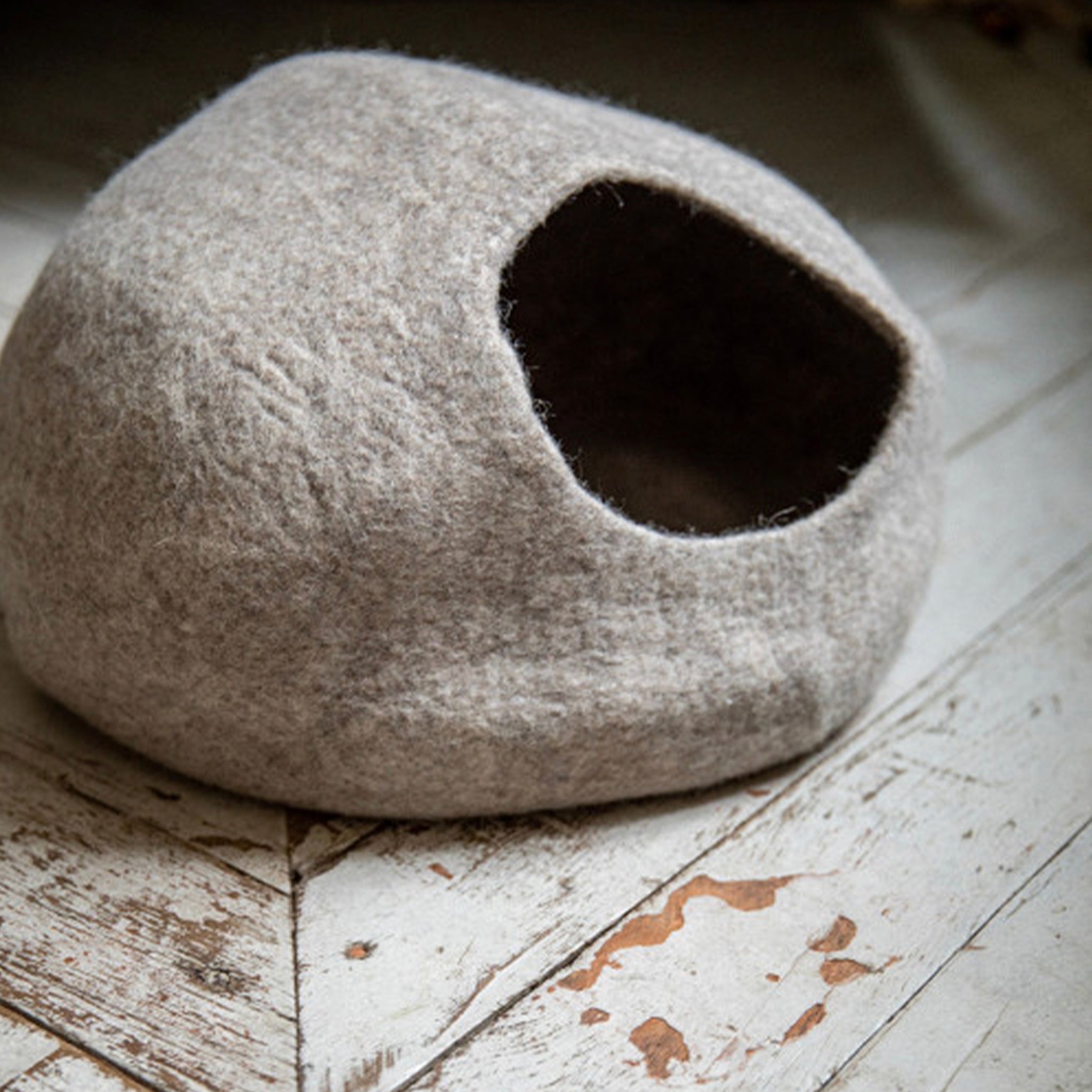 A light stone-colored felt cat basket with an entrance hole on the side.