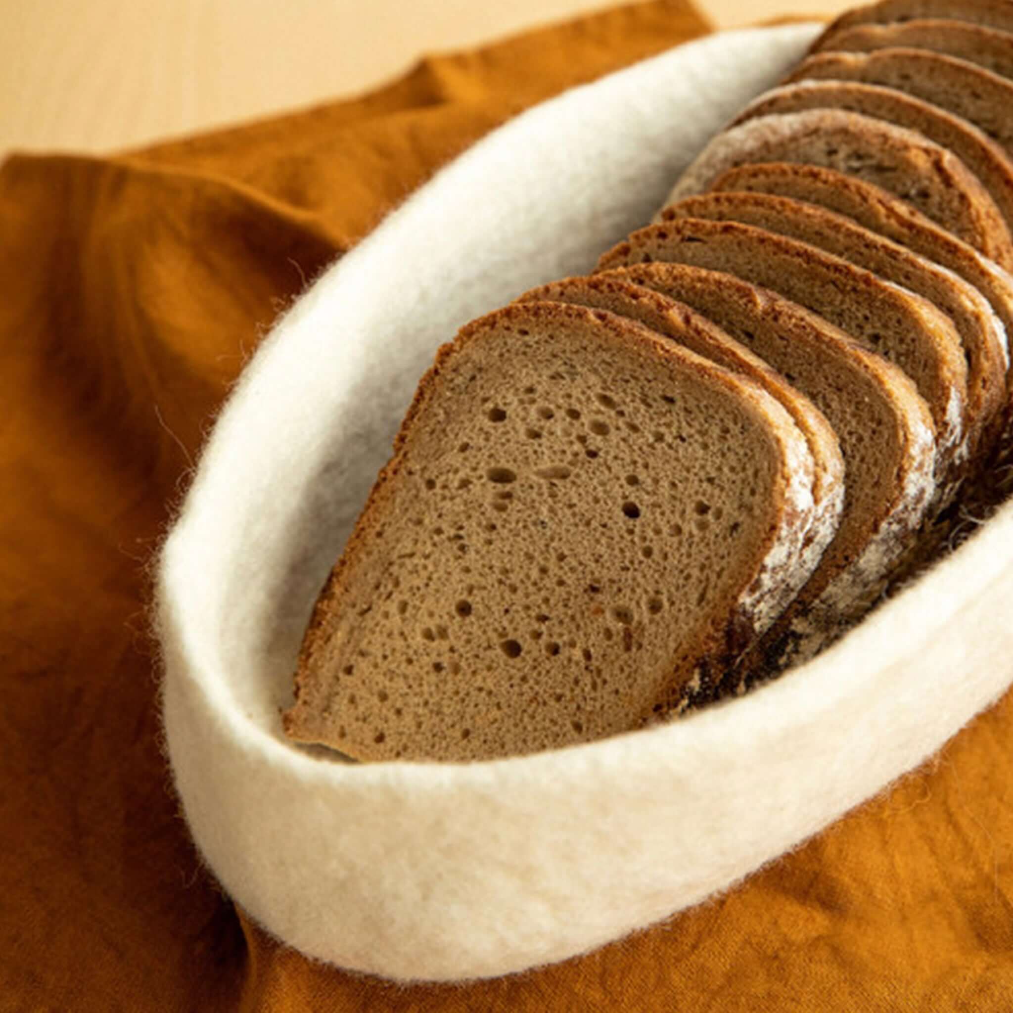 White felt basket with bread on a brown tablecloth.