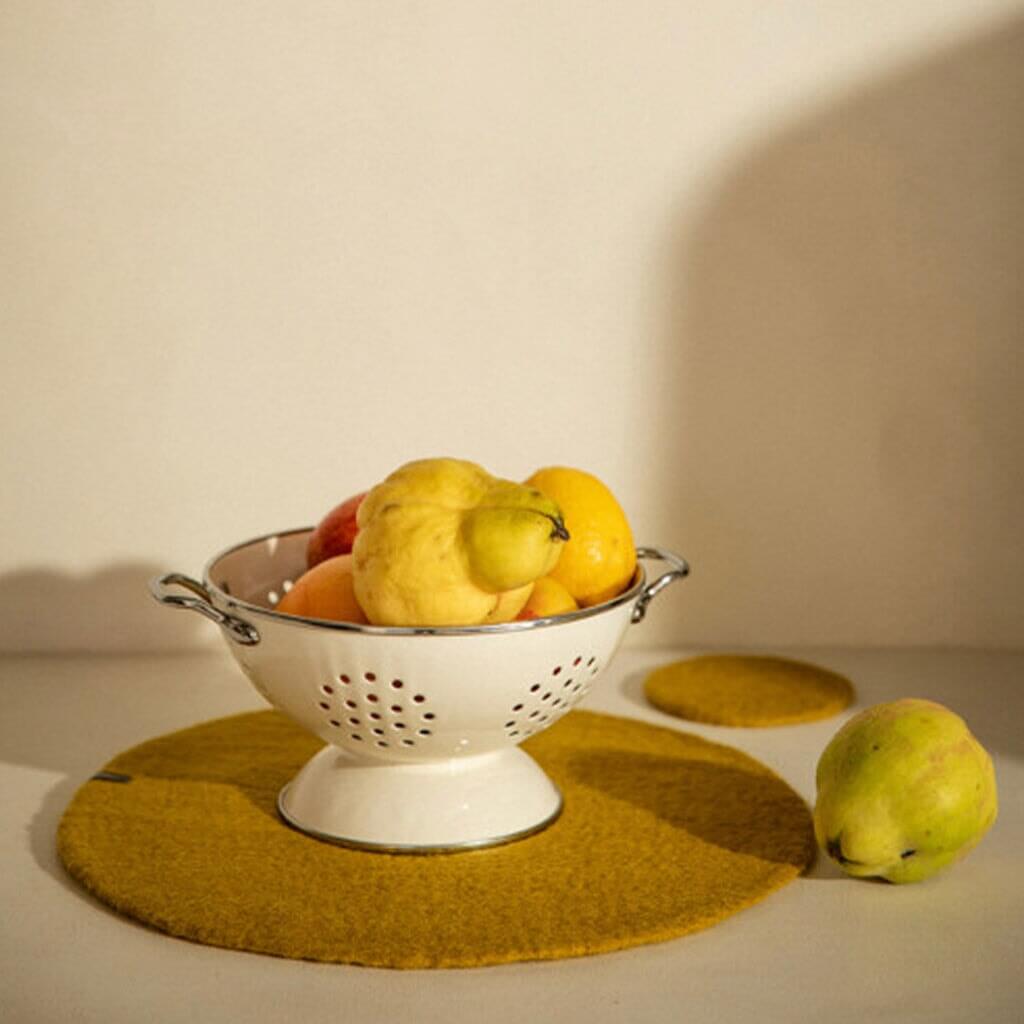Alt Tag: Muskhane Felt Plain Round Placemat - Natural Large round felt placemat with fruit bowl centerpiece on tabletop