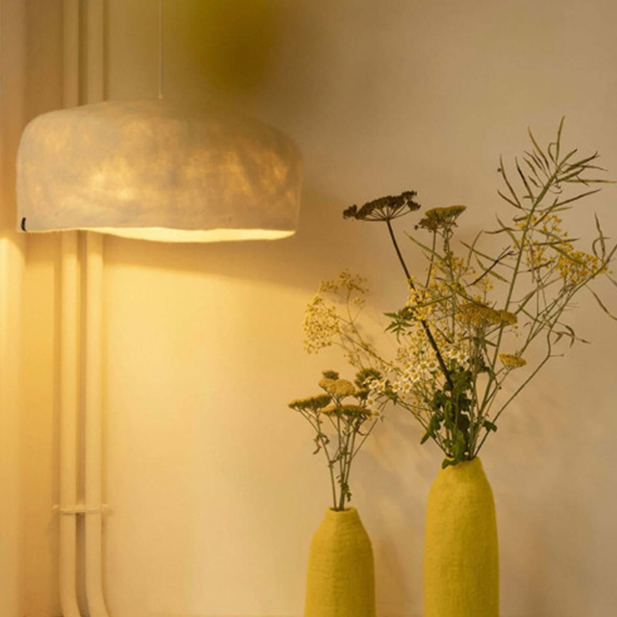 Alt Tag: Muskhane Felt Yurt Lampshade - Natural hanging felt pendant light glowing above vases in a warm, minimalist interior