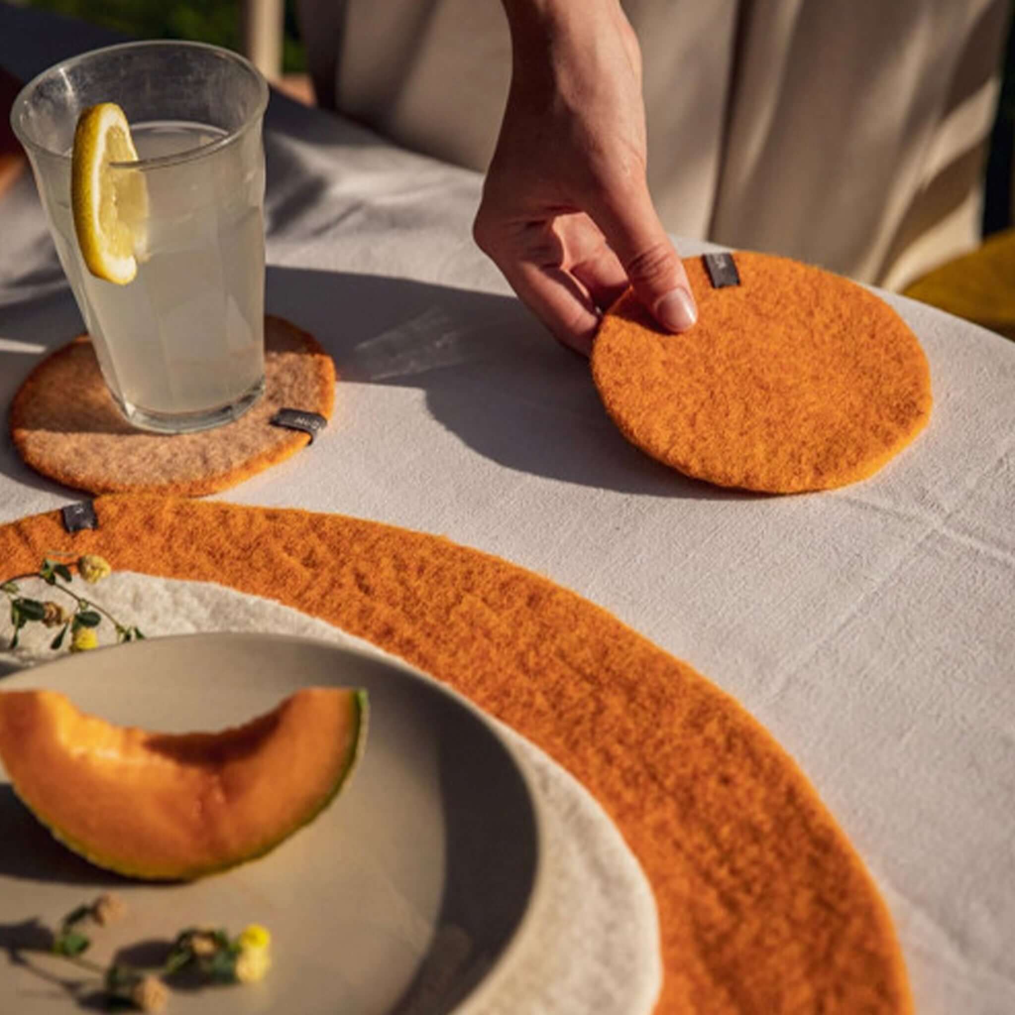 Muskhane Felt Plain Round Coaster - Apricot felt round coaster on table under glass, handmade Nepal Fairtrade, 12cm