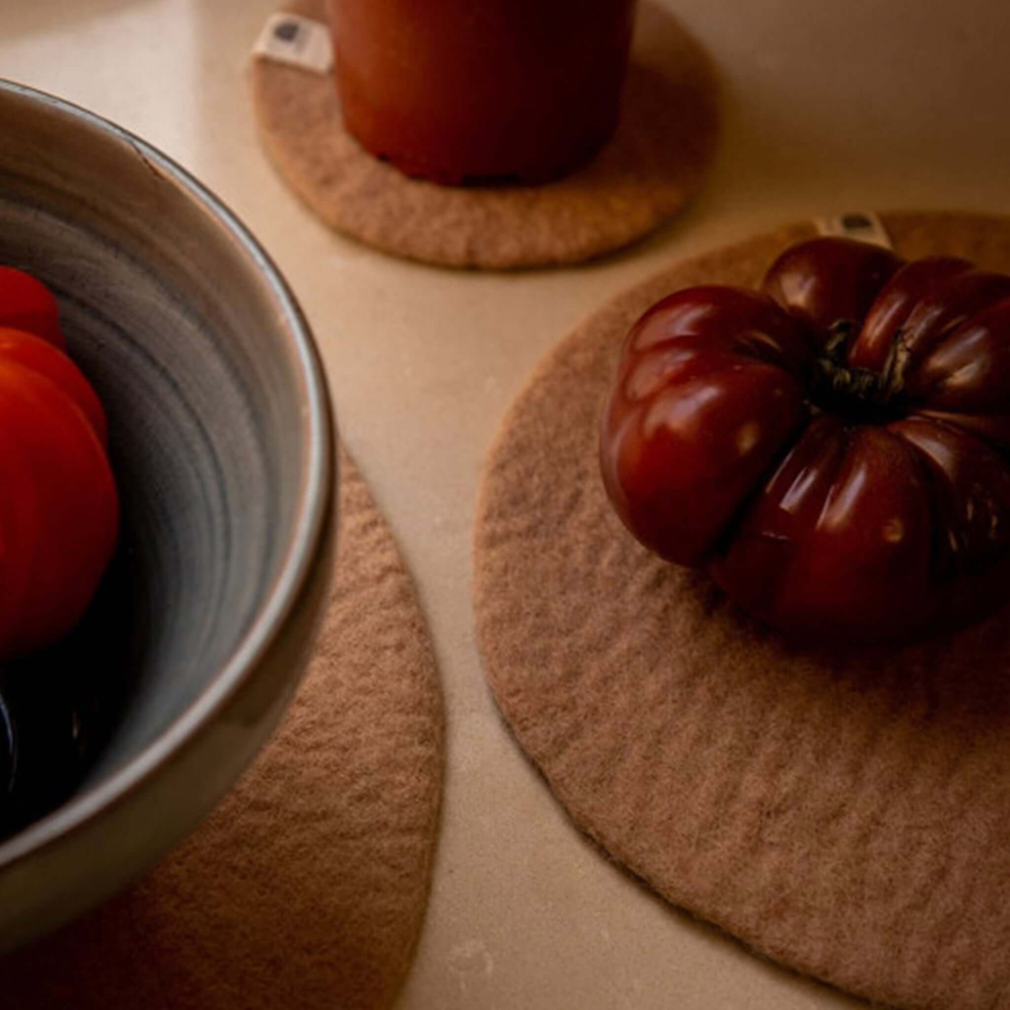 Muskhane Felt Plain Round Placemat - Nude Large used as a trivet with a bowl and fresh tomatoes.