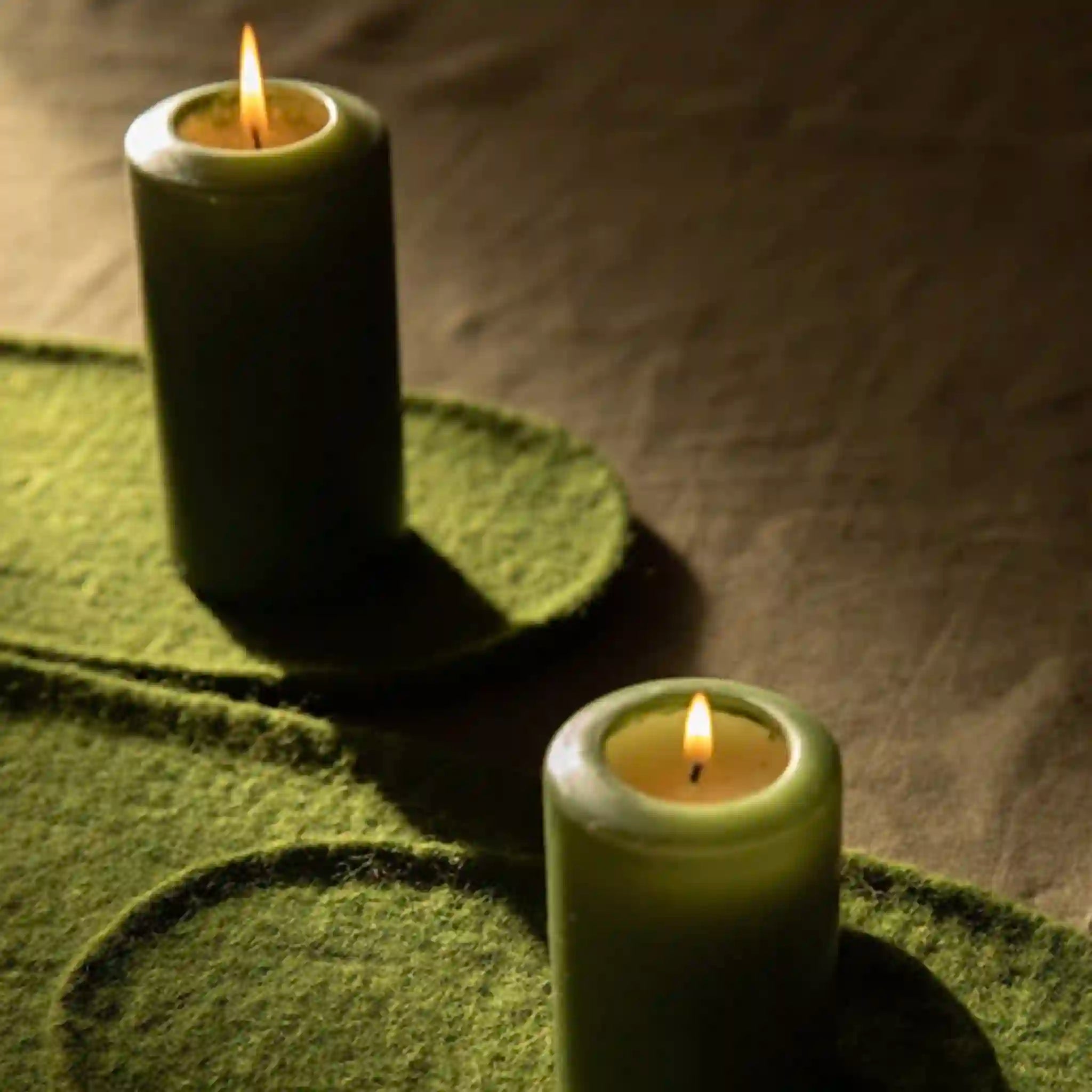 Two green candles on a textured surface with a dark background