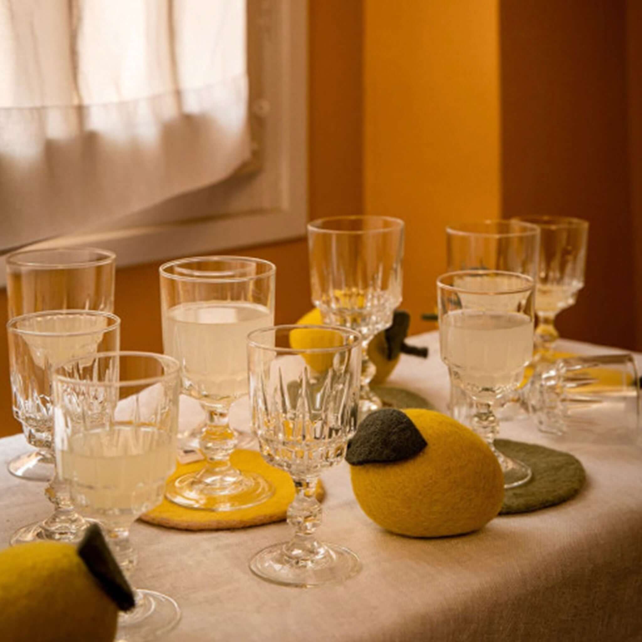 Muskhane Felt Two Tone Round Coaster - Nude & Lemon with glasses and drinks on a table.