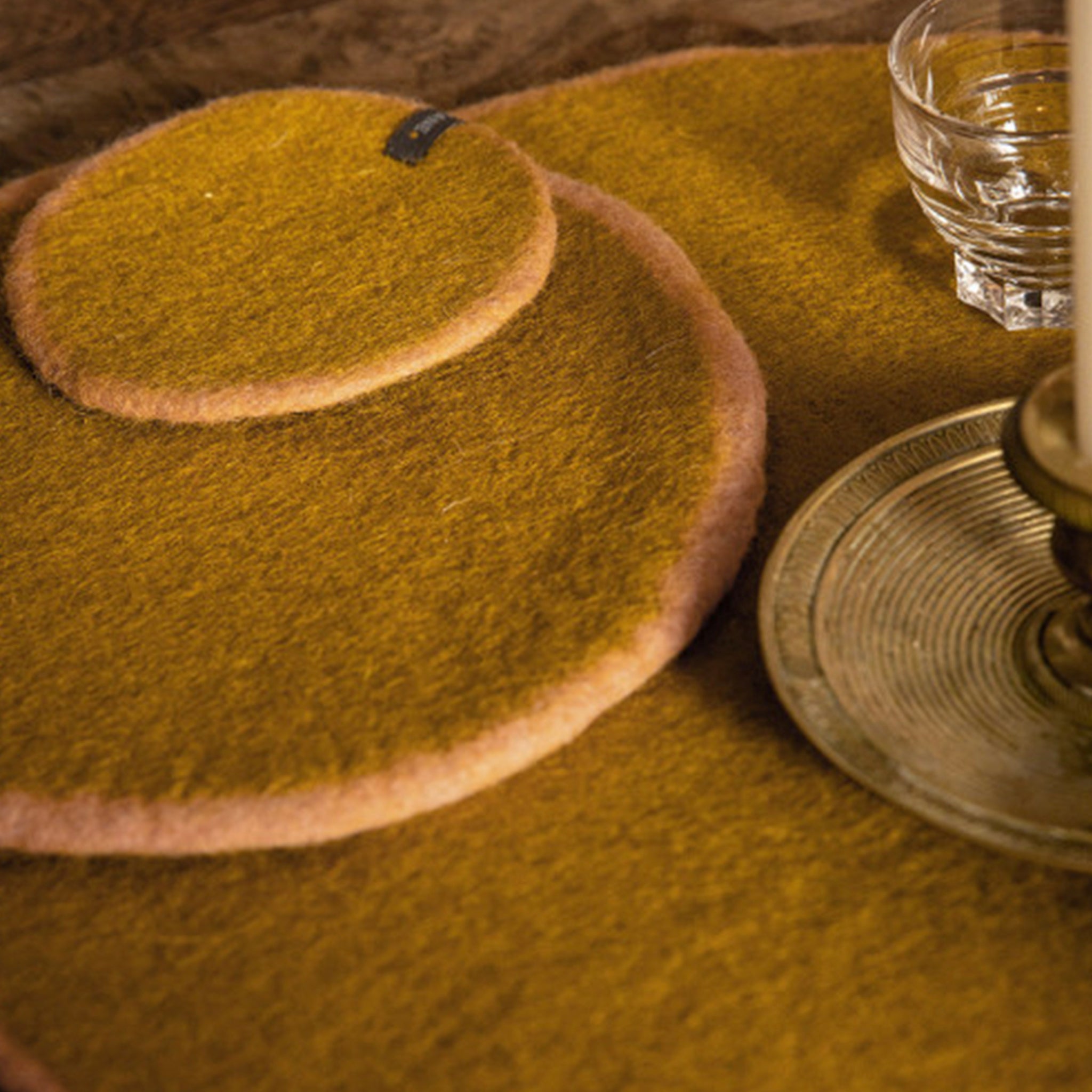 Round green felted coaster and placemats on a table.