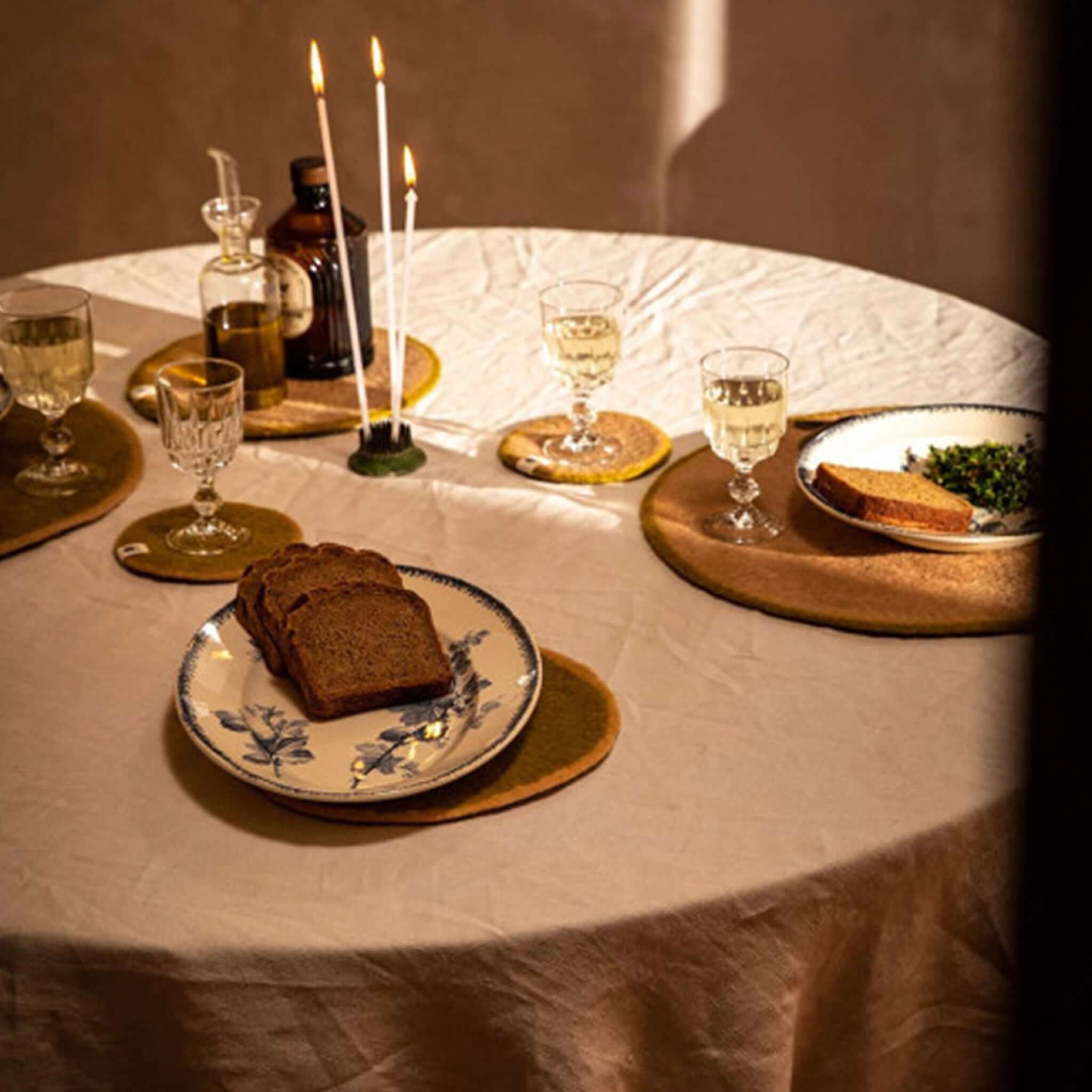 Muskhane Felt Two Tone Round Coaster - Pistachio & Nude placed on a dining table setting with plates and glasses.
