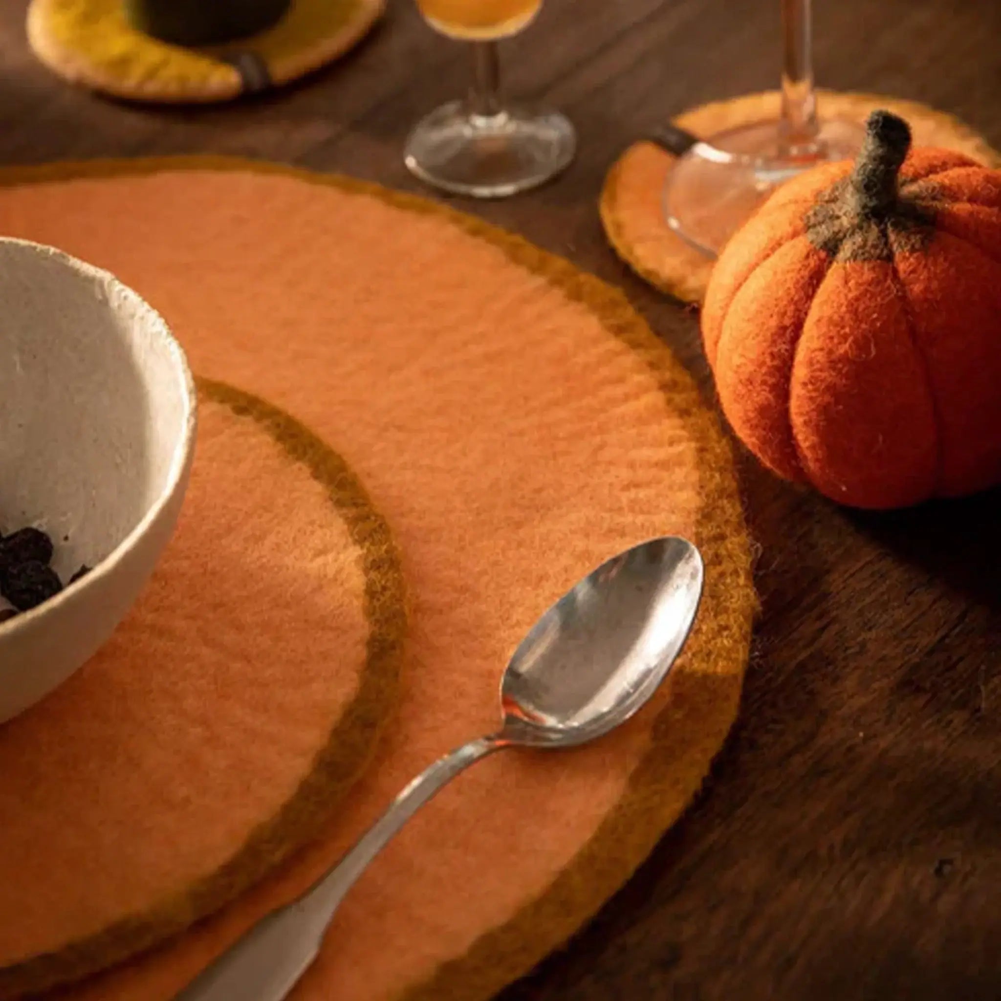 Alt Tag: Muskhane Felt Two Tone Round Placemat - Apricot & Nude Large on wooden table with spoon, bowl and pumpkin decor