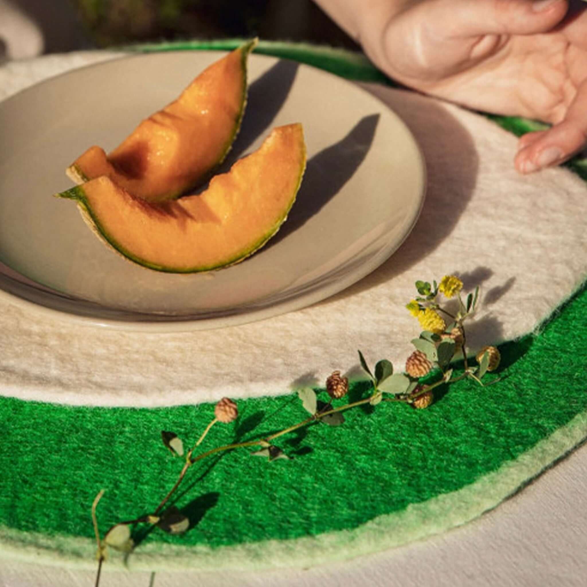 Alt Tag: Muskhane Felt Two Tone Round Placemat - Green & Mint under plate with melon slices, showcasing two-tone felt table mat