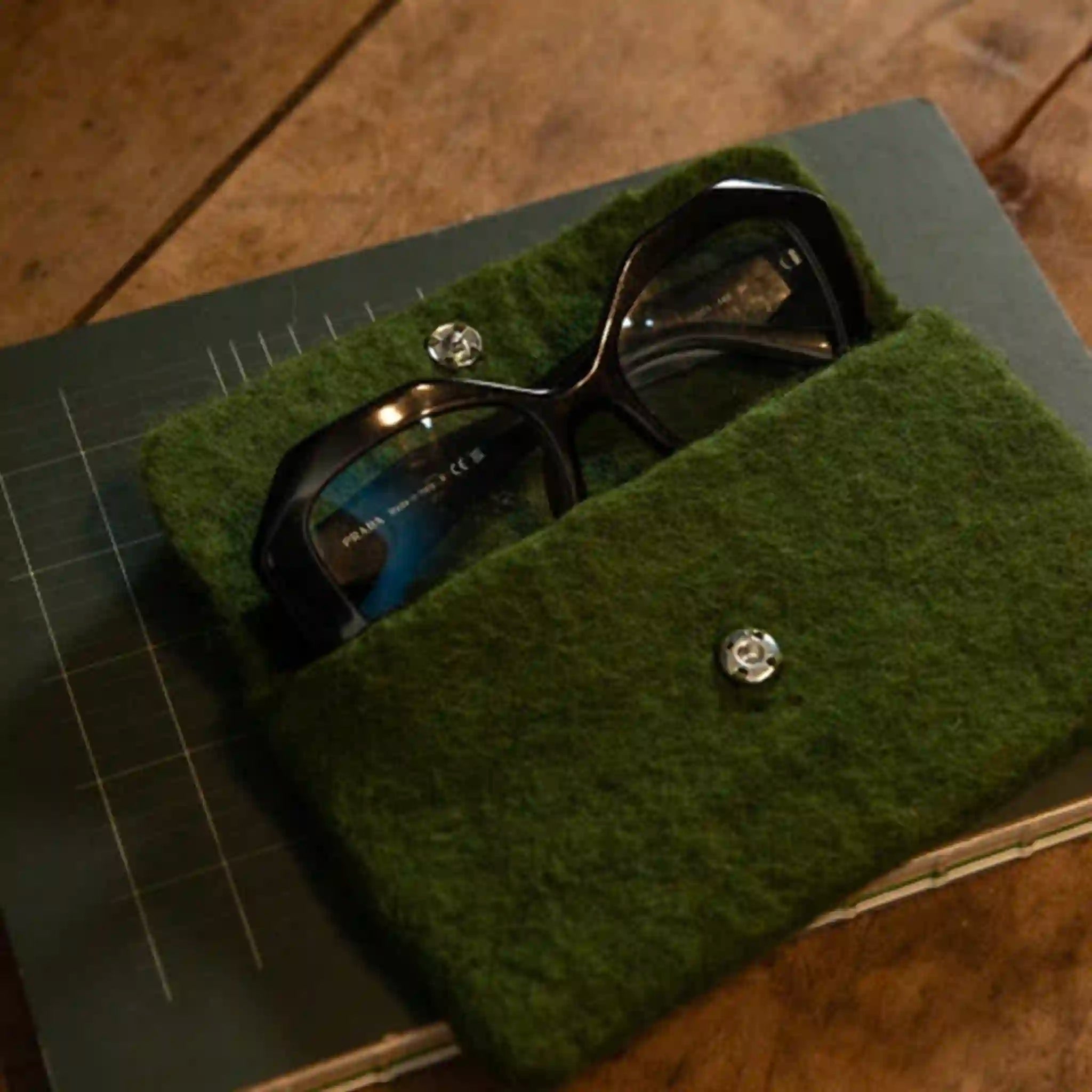 Green felt sunglasses case with sunglasses on a wooden surface