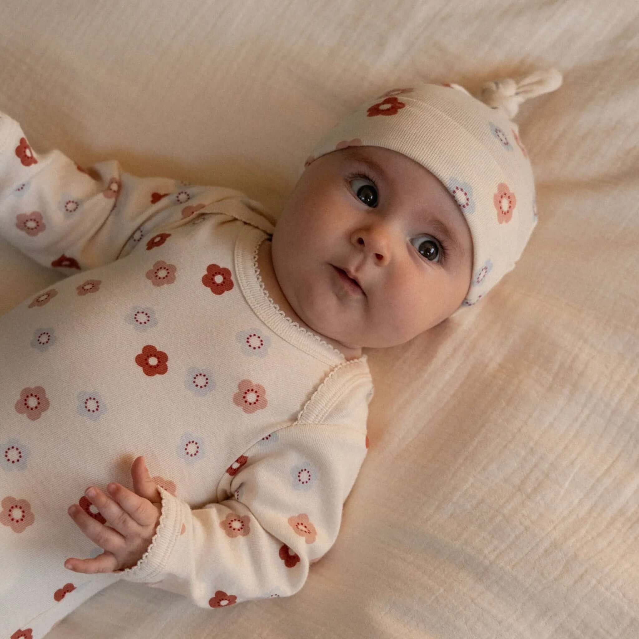Nature Baby Organic Cotton Knotted Beanie - Petite Flora Stamp on a baby, showcasing soft organic cotton and cute floral design.