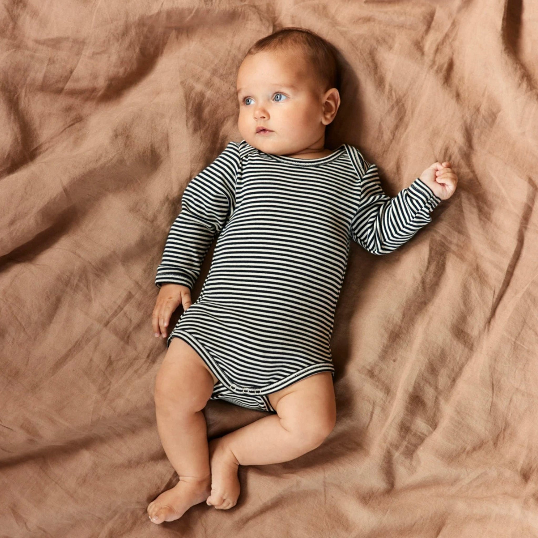 Baby wearing a navy and white striped baby bodysuit on a brown sheet.