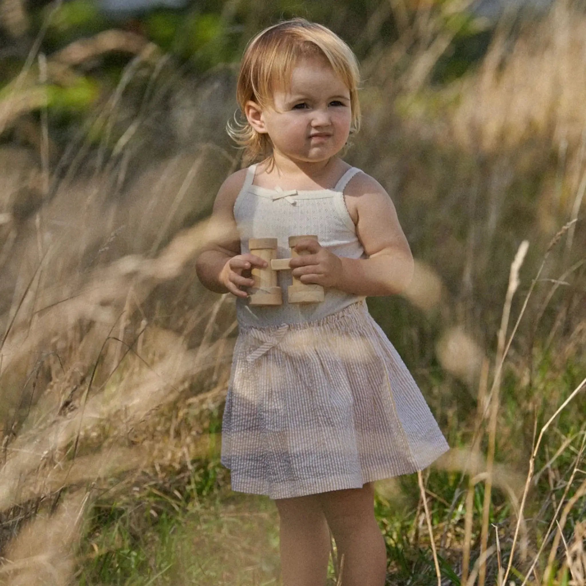 Alt Tag: Nature Baby Organic Cotton Orchard Skirt - Golden Stripe toddler wearing organic cotton skirt outdoors with gathered waist and bow
