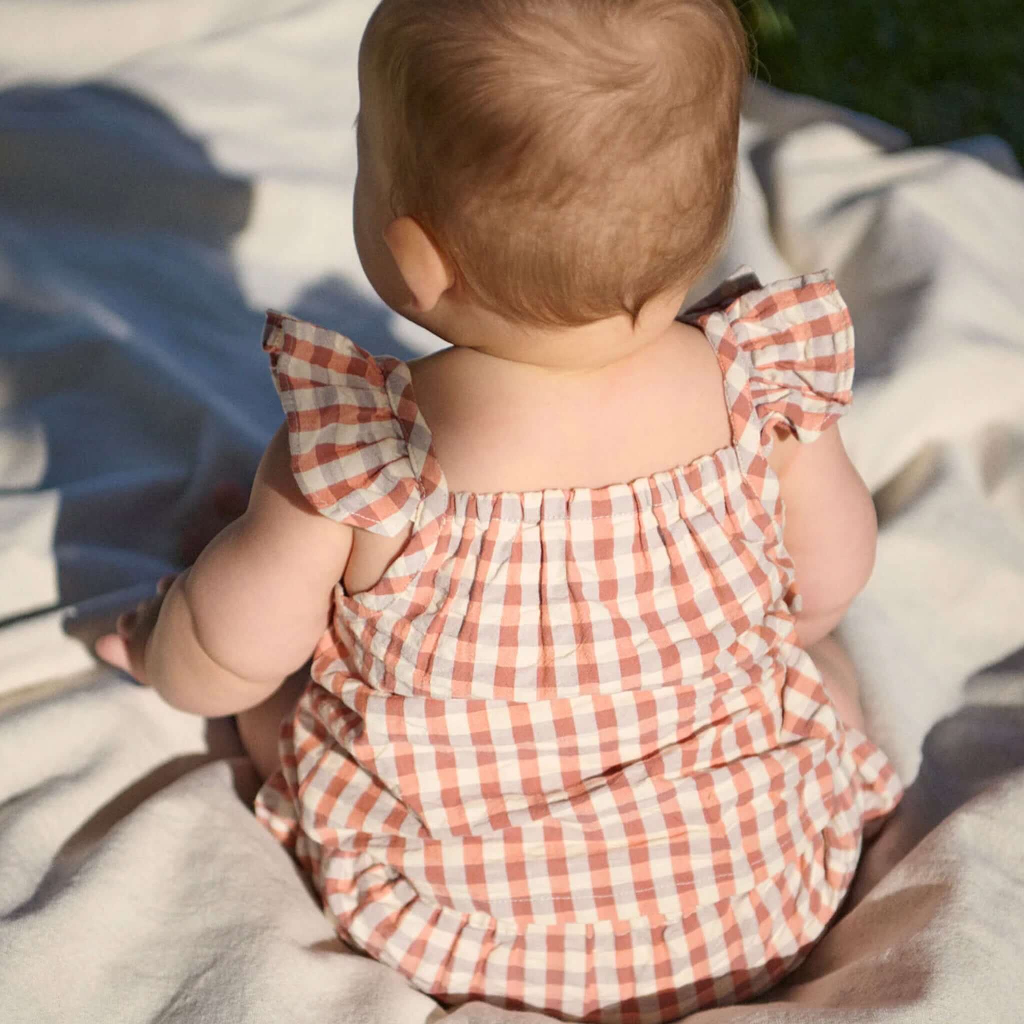 Nature Baby Organic Cotton Petal Set - Dandelion Gingham on a baby sitting on a soft blanket, showcasing frill details.