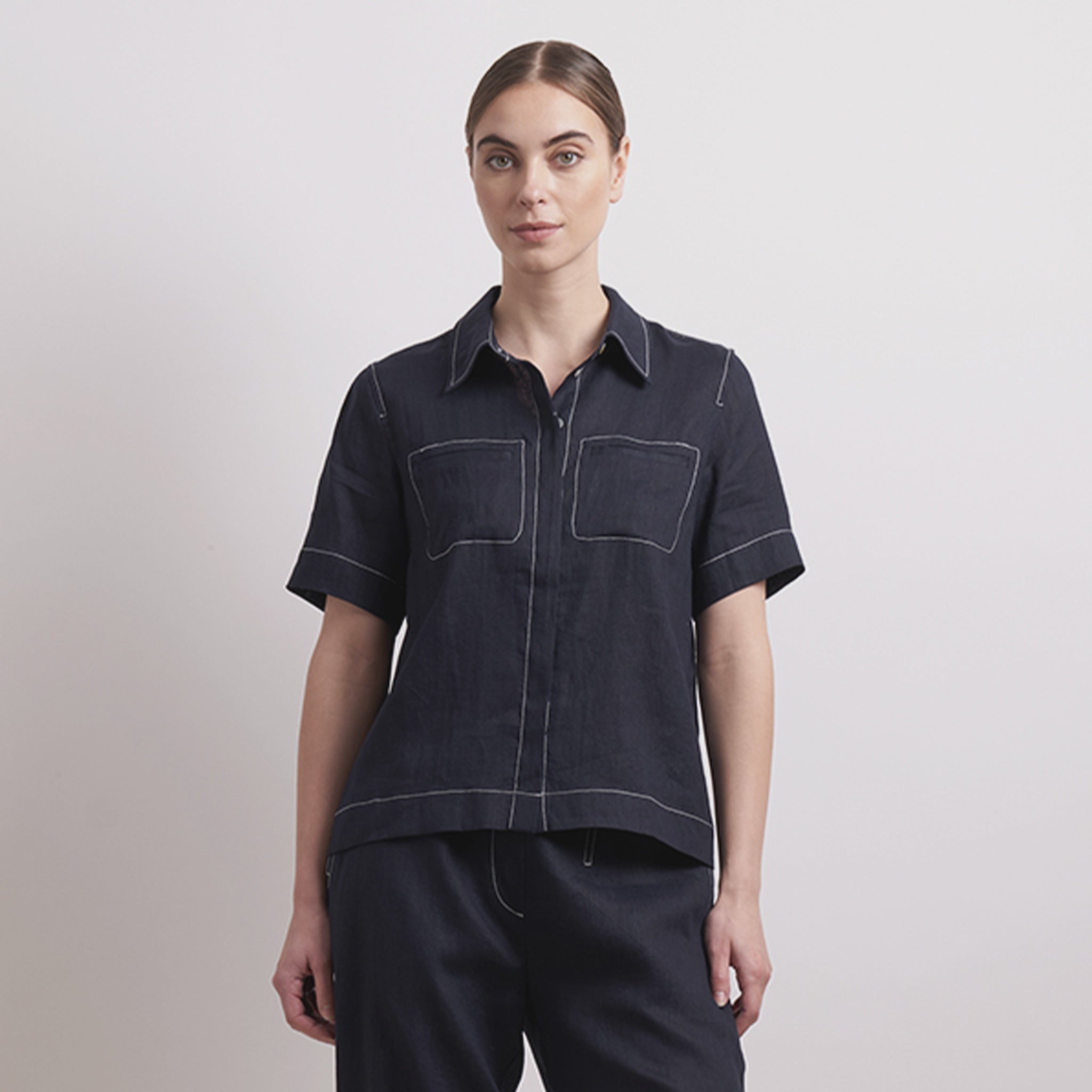 Woman wearing a dark denim shirt with white stitching on a light gray background