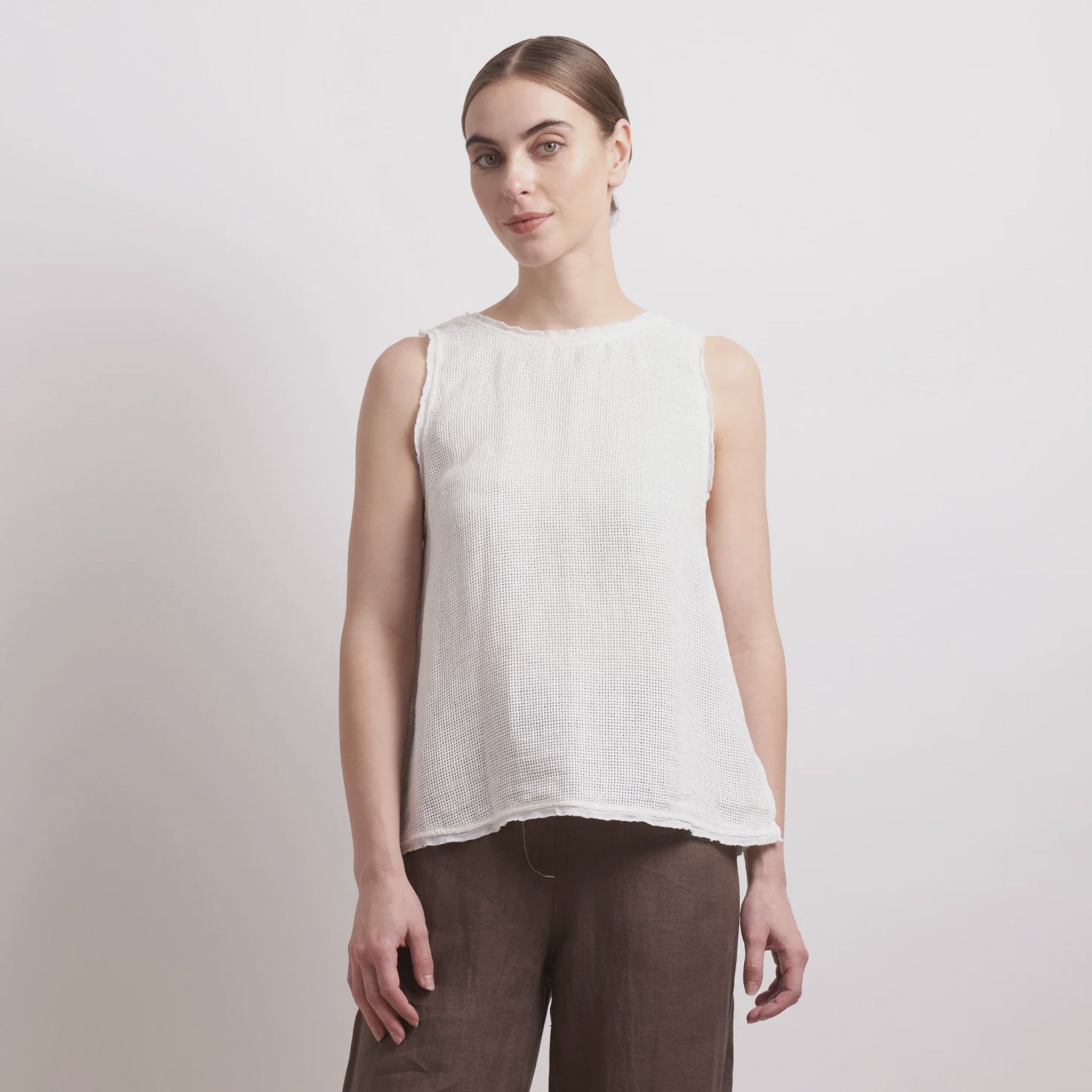 Woman wearing a white sleeveless top and brown pants on a light background