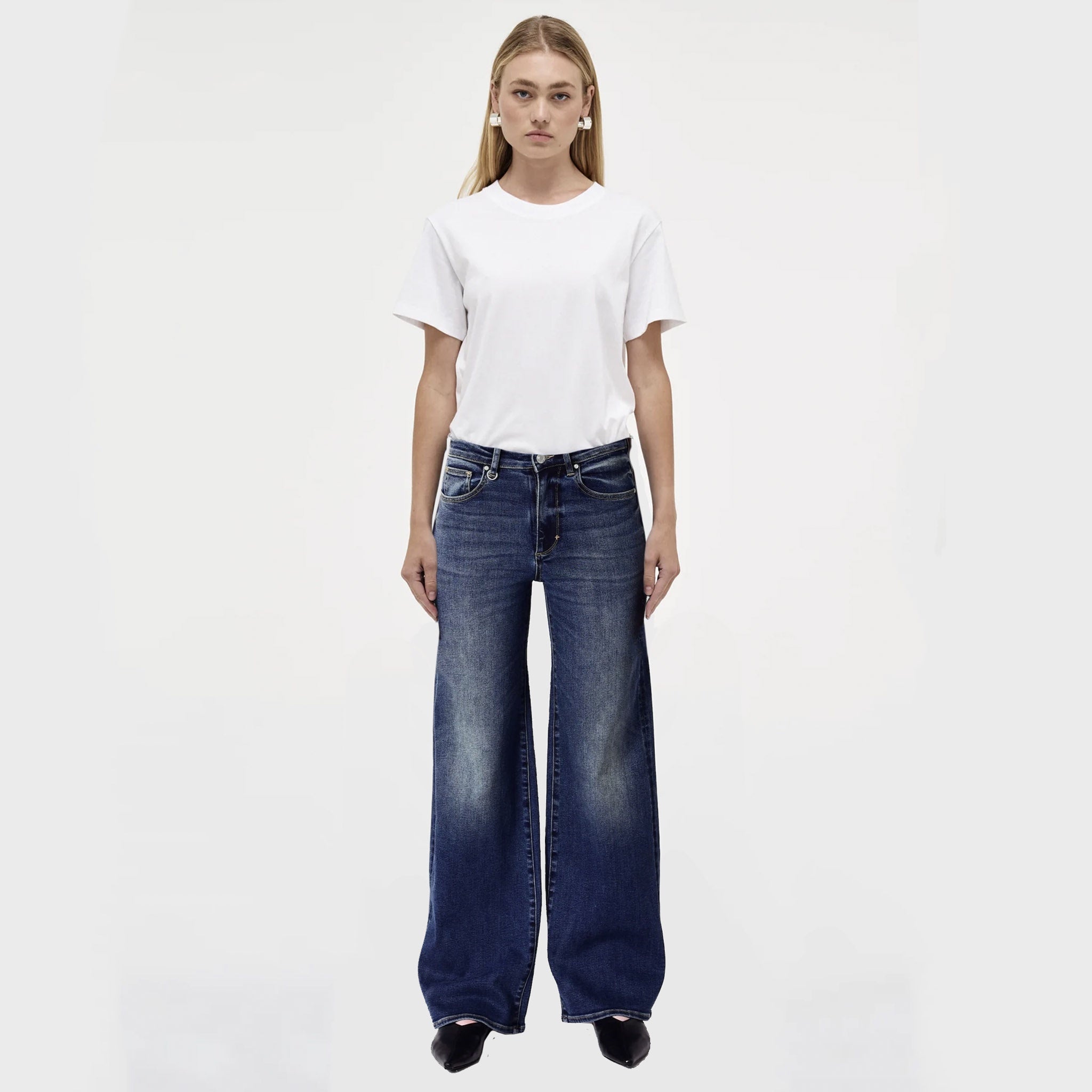 A female model wearing a white t-shirt and wide leg indigo blue jeans.
