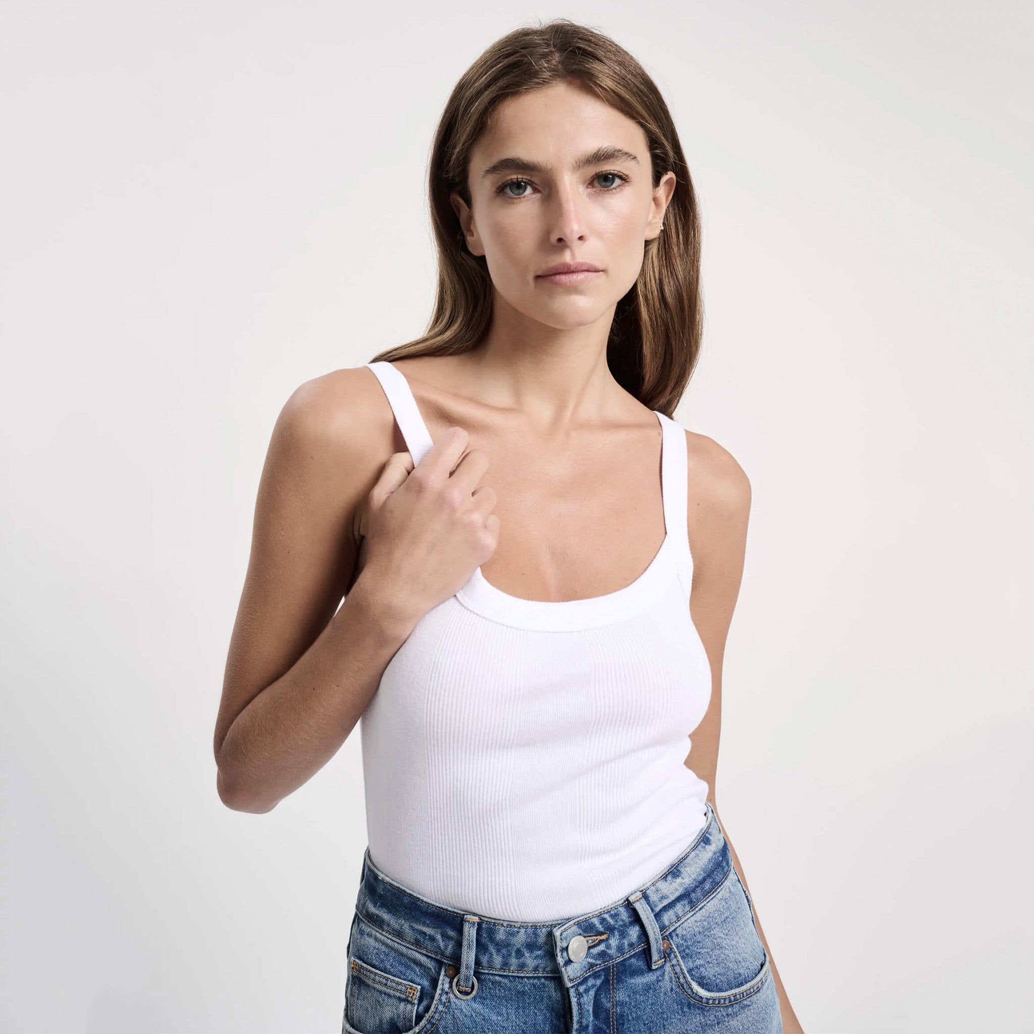 A female model wearing a white organic cotton rib singlet with a flattering slim fit, paired with blue denim shorts.