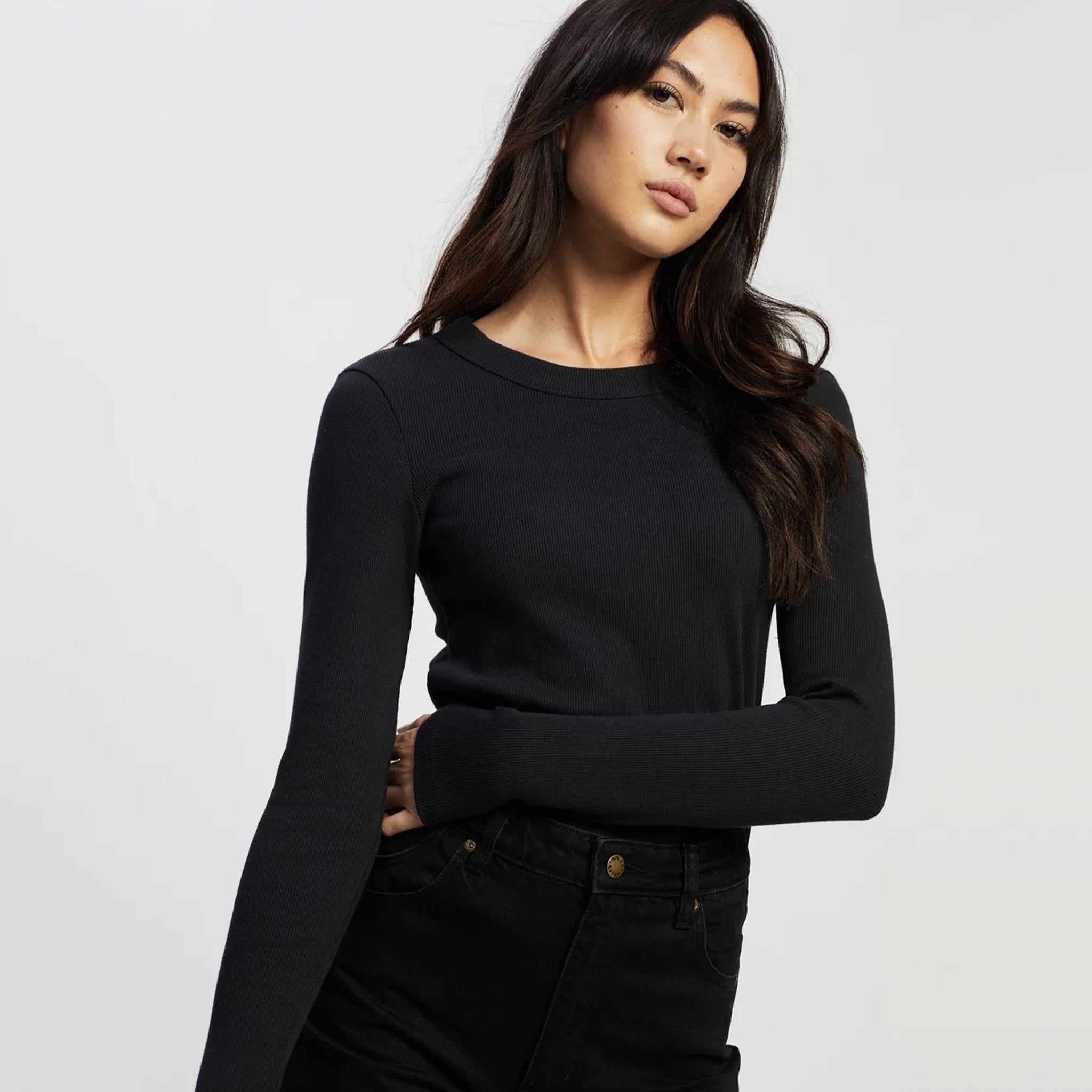 A person wearing a black long-sleeve top made from organic cotton, posing against a white background.