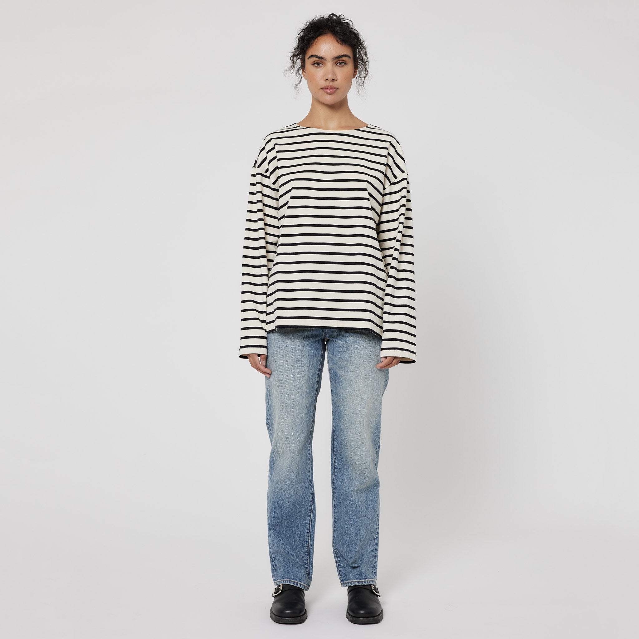 A person wearing a black and white striped top and blue jeans, standing against a white background.