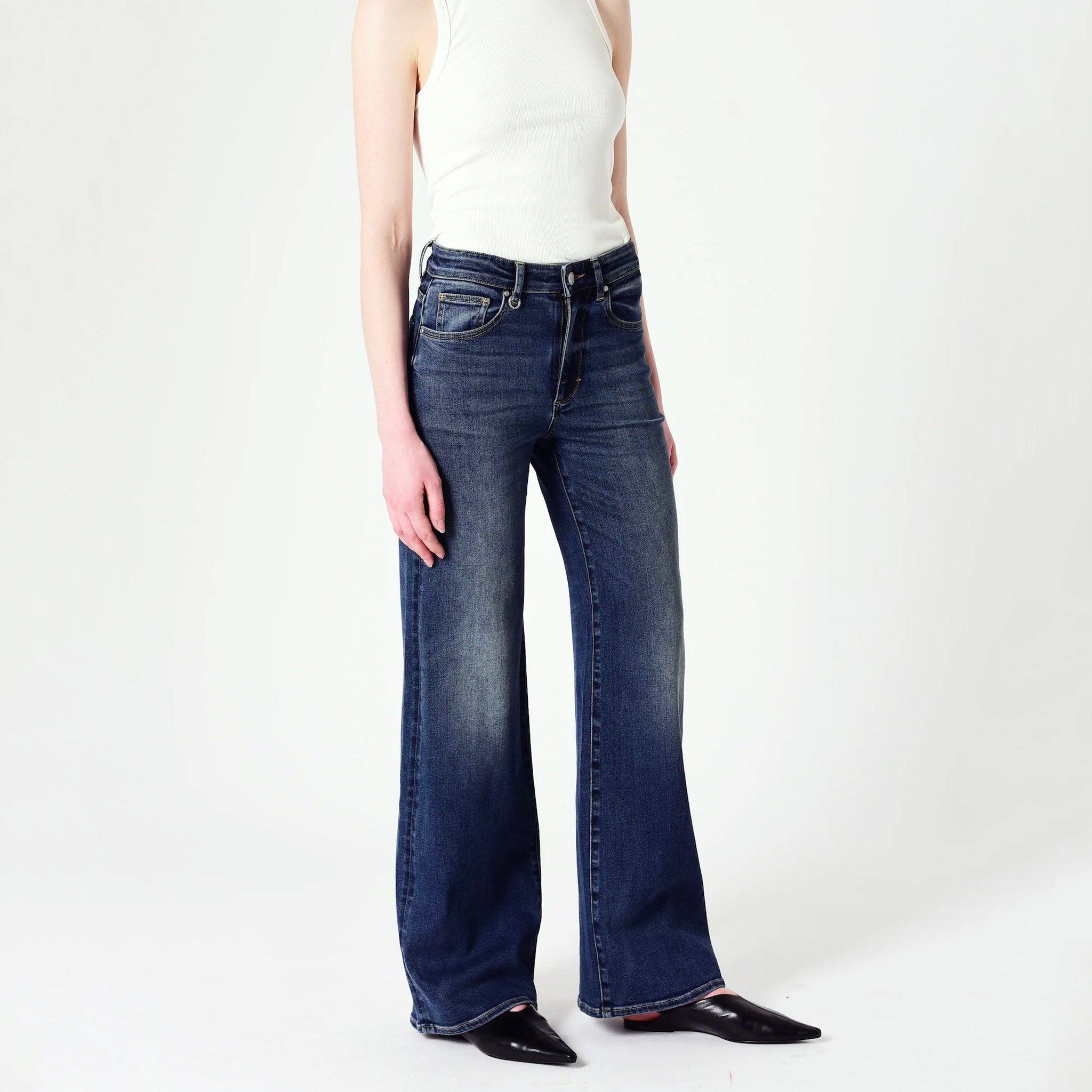 A female model wearing a white t-shirt and wide leg indigo blue jeans.
