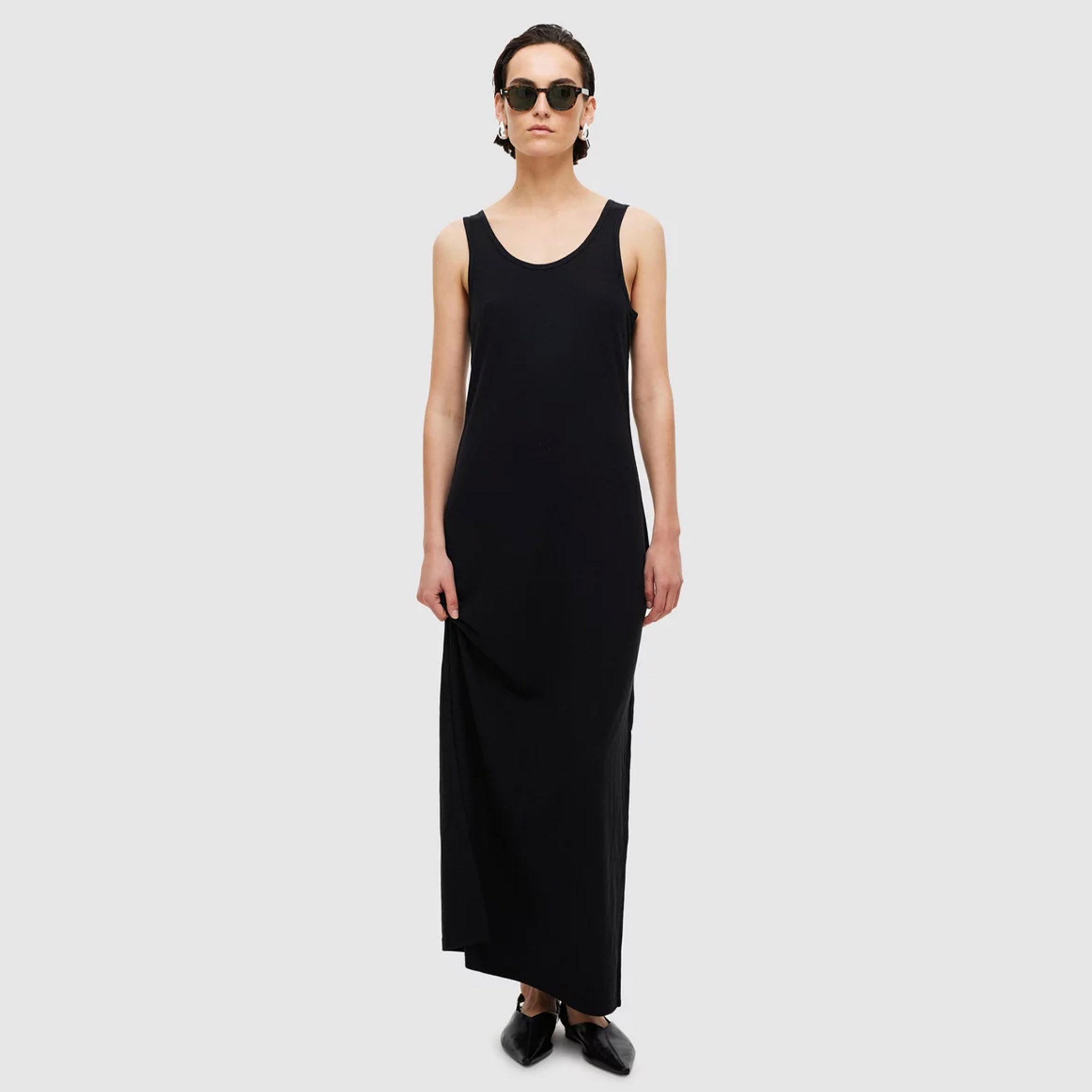 A model wearing a black maxi-length tank dress with a scoop neckline and tank-style straps.