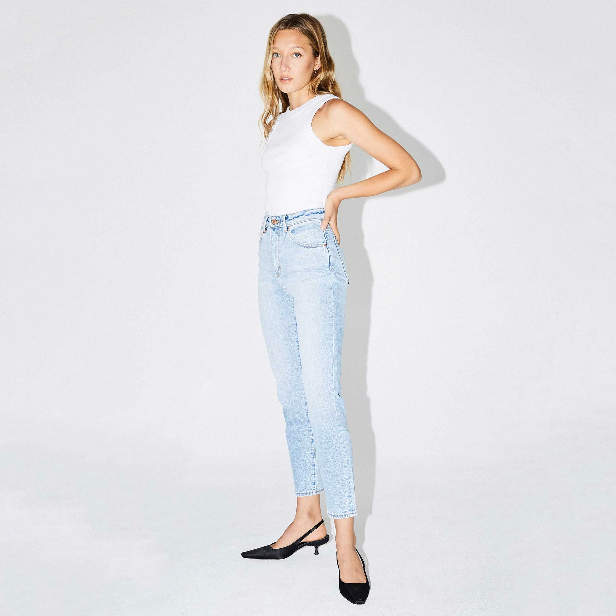 A person wearing a white strapless top and blue jeans, standing against a white background.