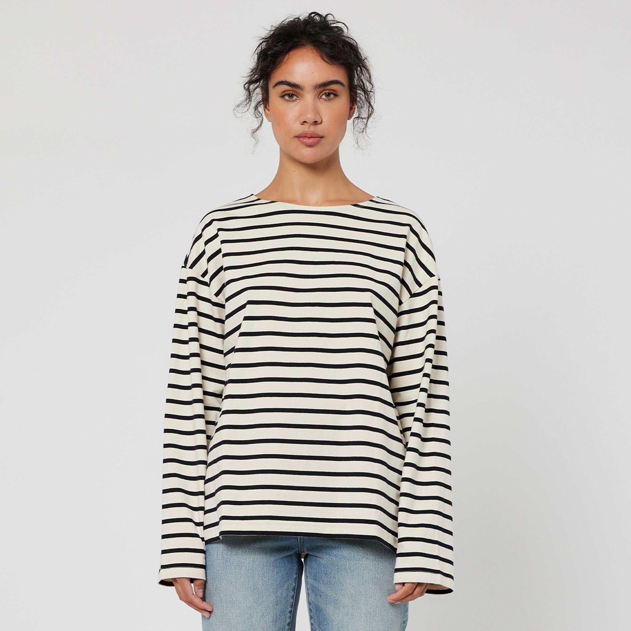 A person wearing a black and white striped top and blue jeans, standing against a white background.
