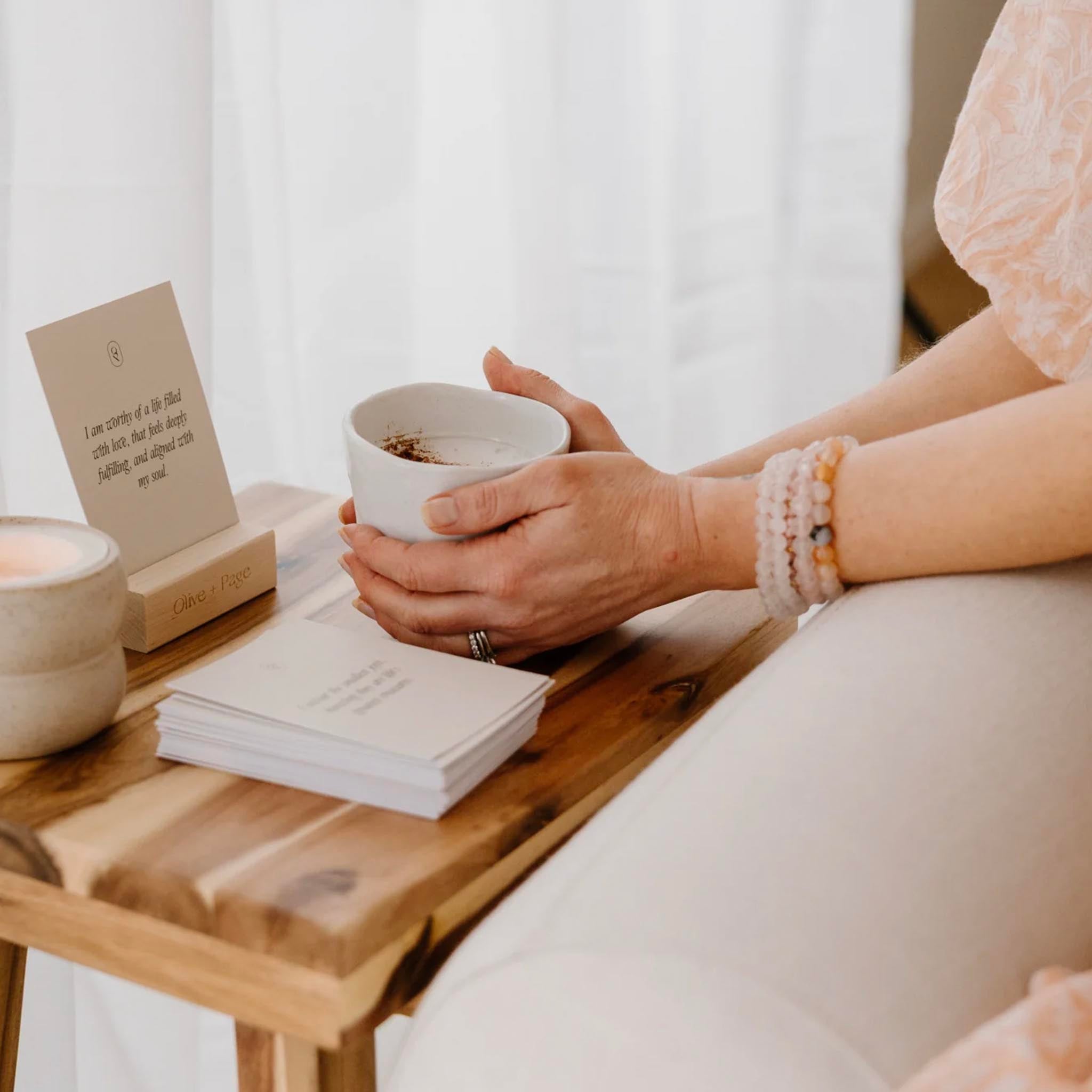 Person holding a white mug with a wooden table and books in the background