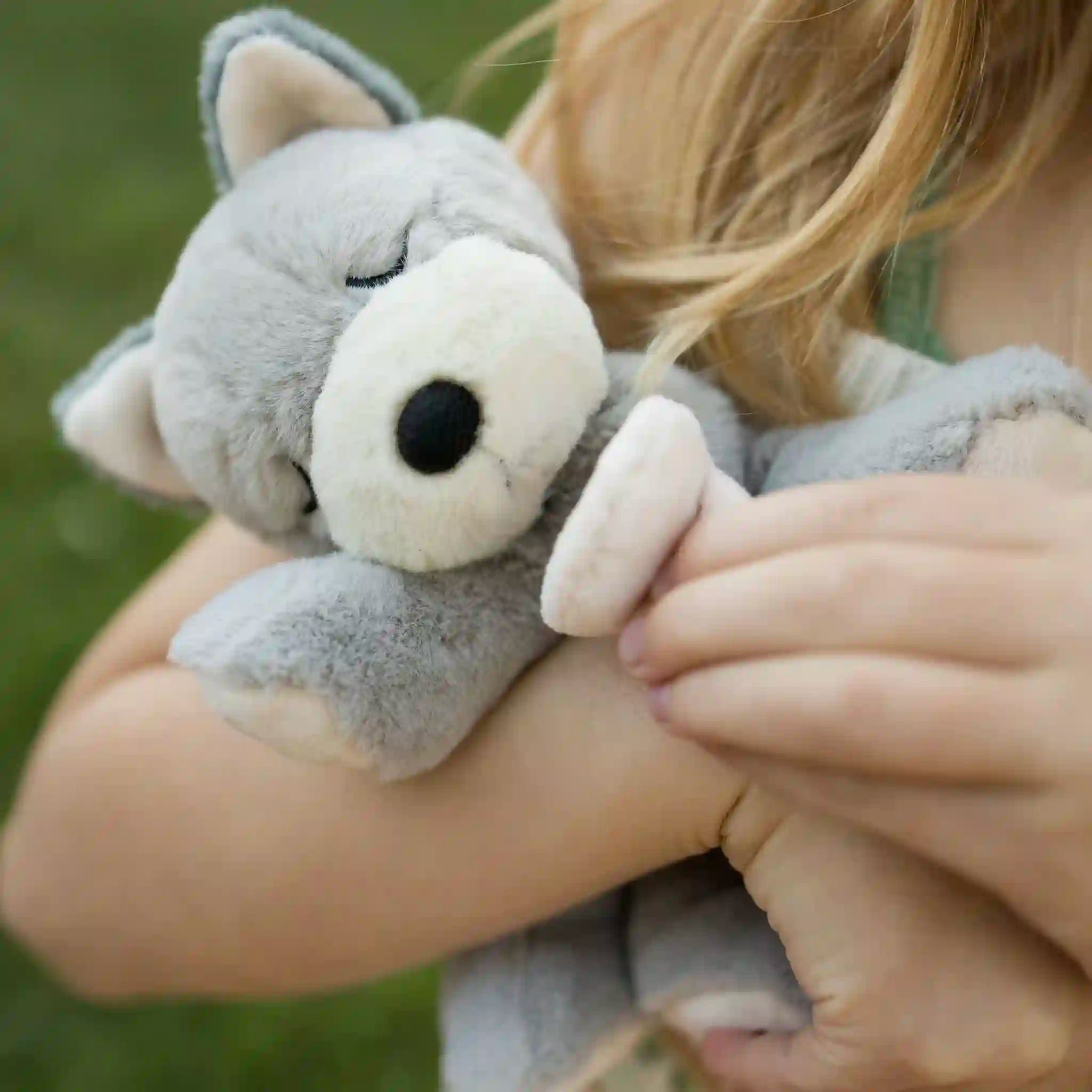 Child holding a plush wolf toy against a blurred green background