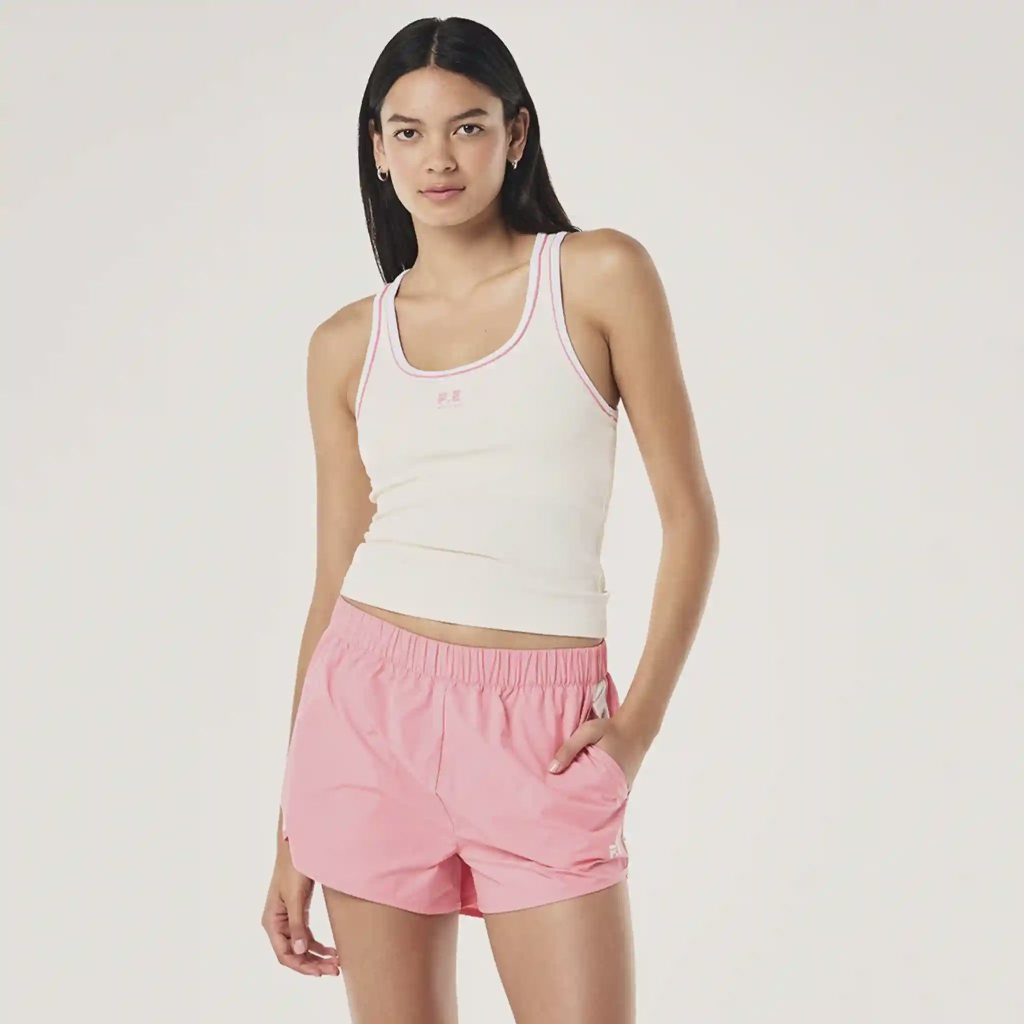 Woman wearing a white tank top and pink shorts on a plain background